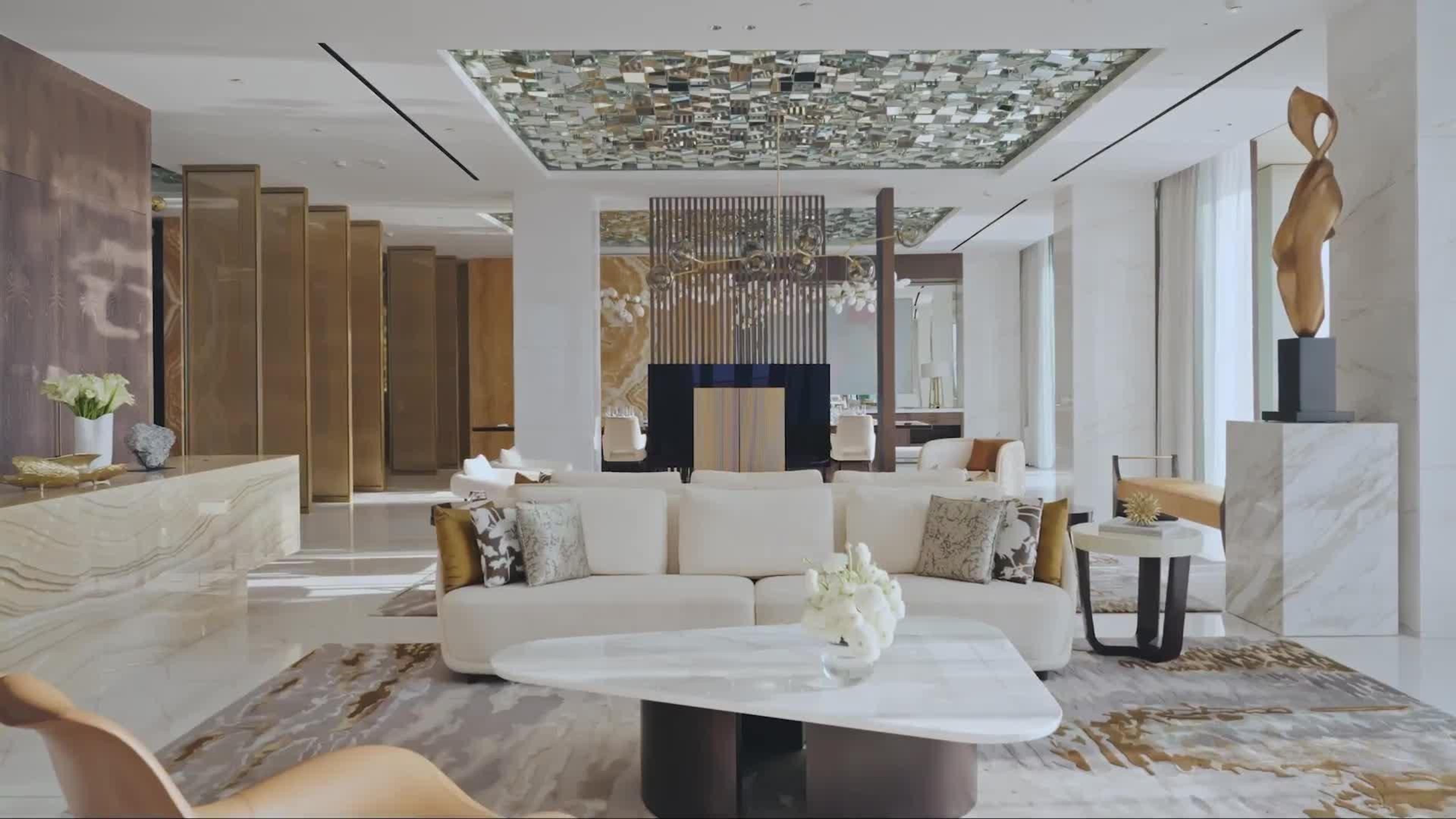 A hotel bedroom with a white bed, a wood accent wall, and a sitting area in front of a floor-to-ceiling window over the water.