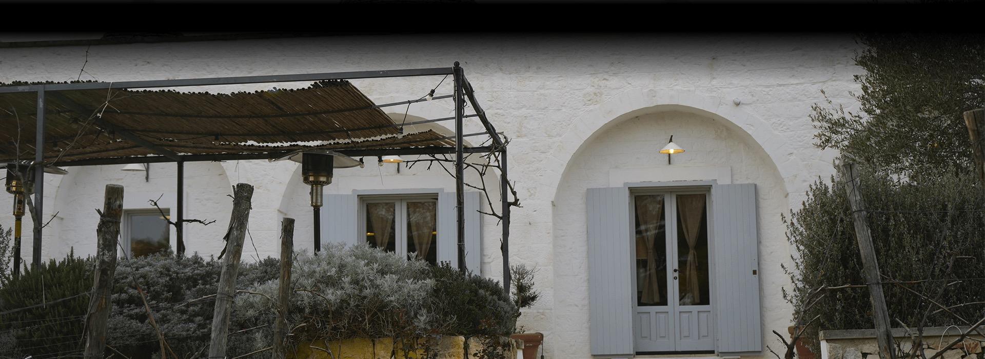 The whitewashed front of Bros' Trattoria under a pergola, its shuttered windows lit at dusk