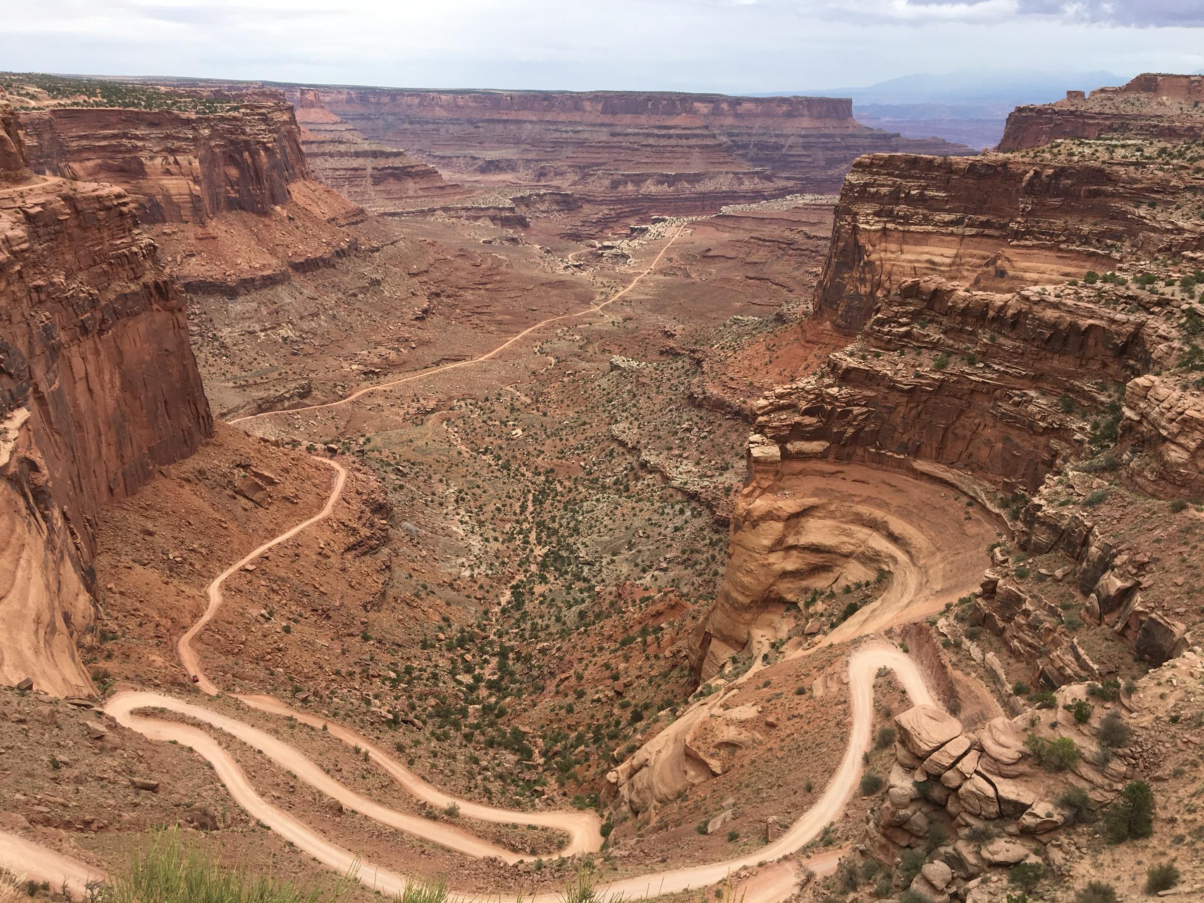 A dirt road zigzagging down a steep red canyon wall
