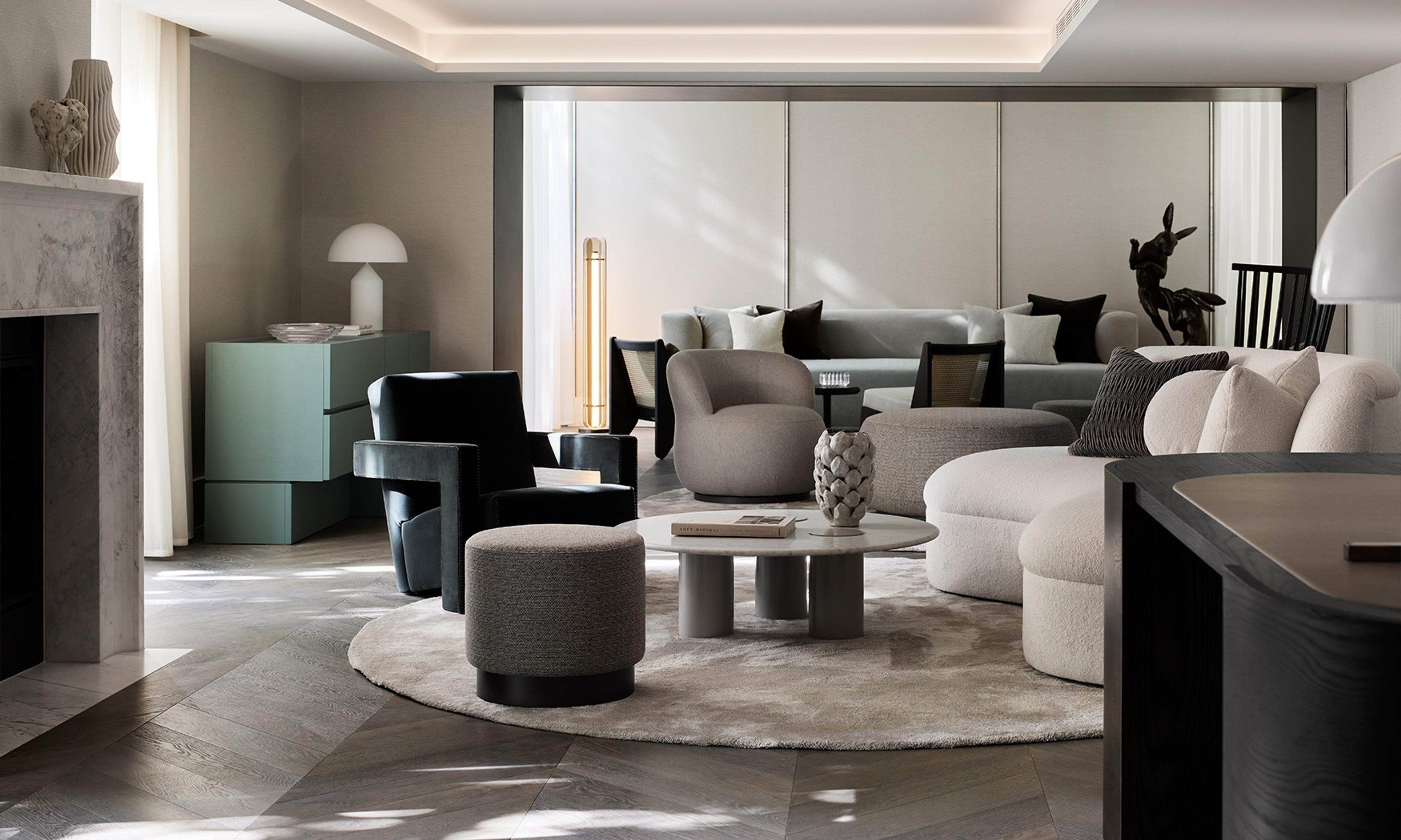 A living room with a marble fireplace, a sage green credenza, grey sofas and a bronze sculpture of rabbits under a coffered ceiling.