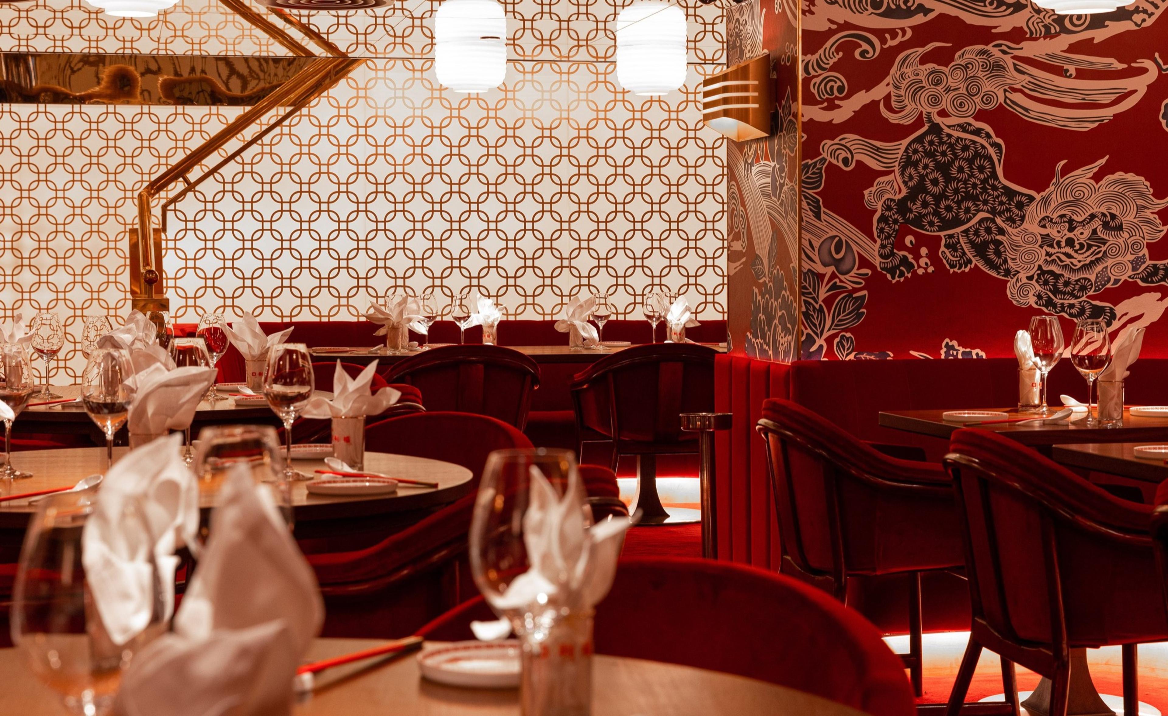A dining room in deep red with patterned wallpaper and round tables