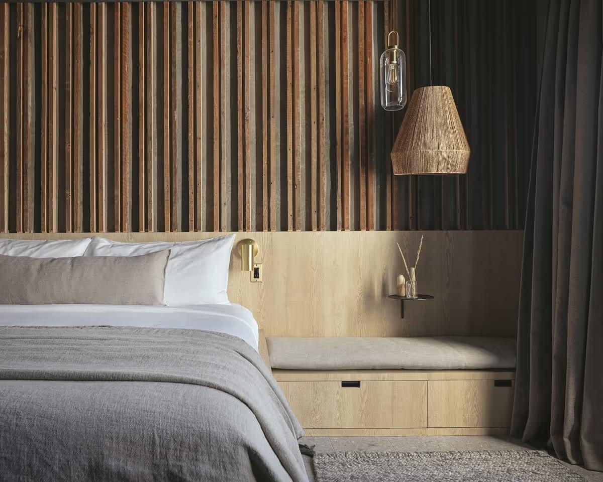 A hotel bedroom with a wood platform bed against a dark wall, seen beside a large window showing the Santa Barbara hills and rooftops beyond.