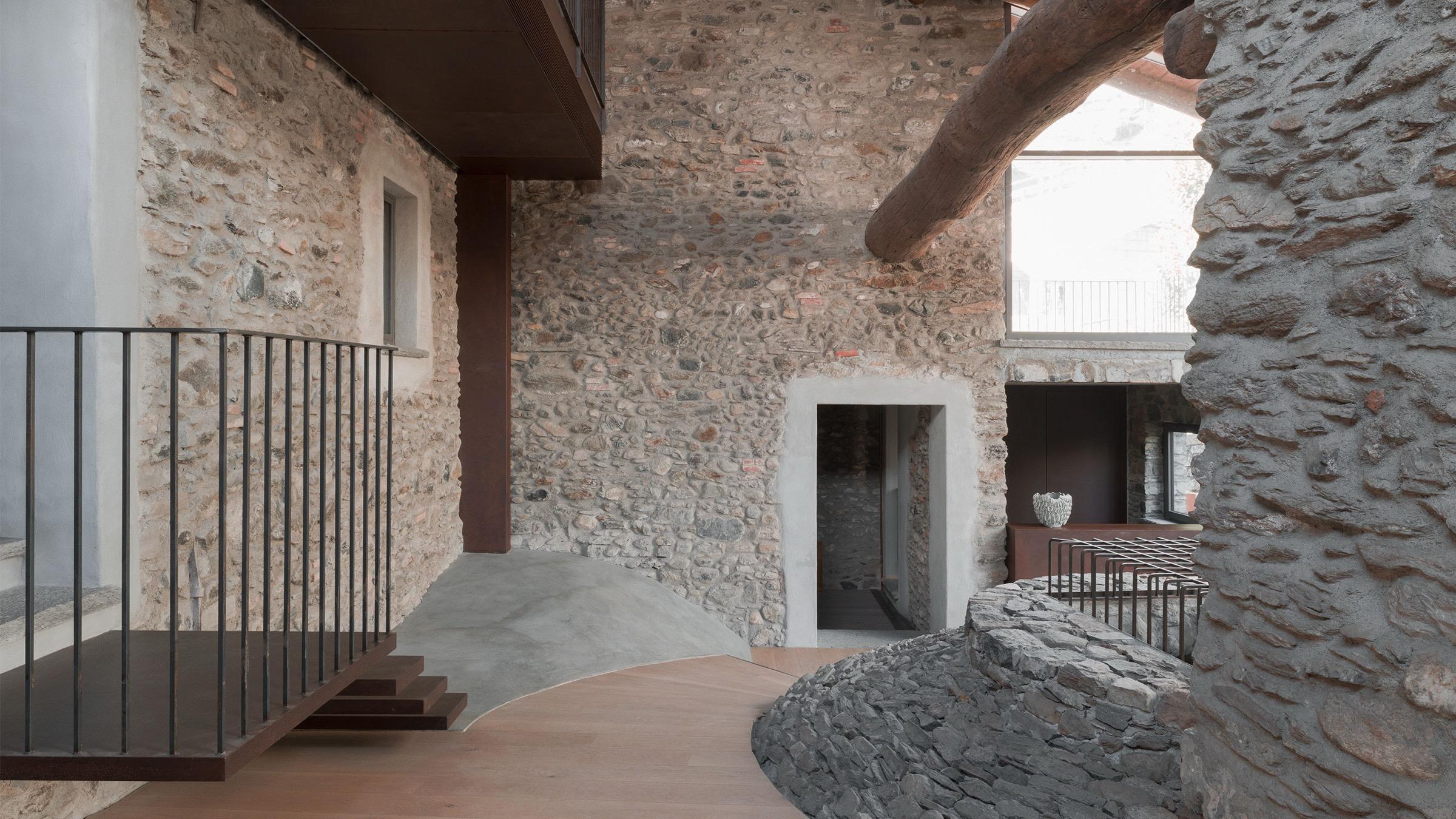 a stone stairwell and landing inside the building, with a wooden beam overhead and a dark modern staircase below