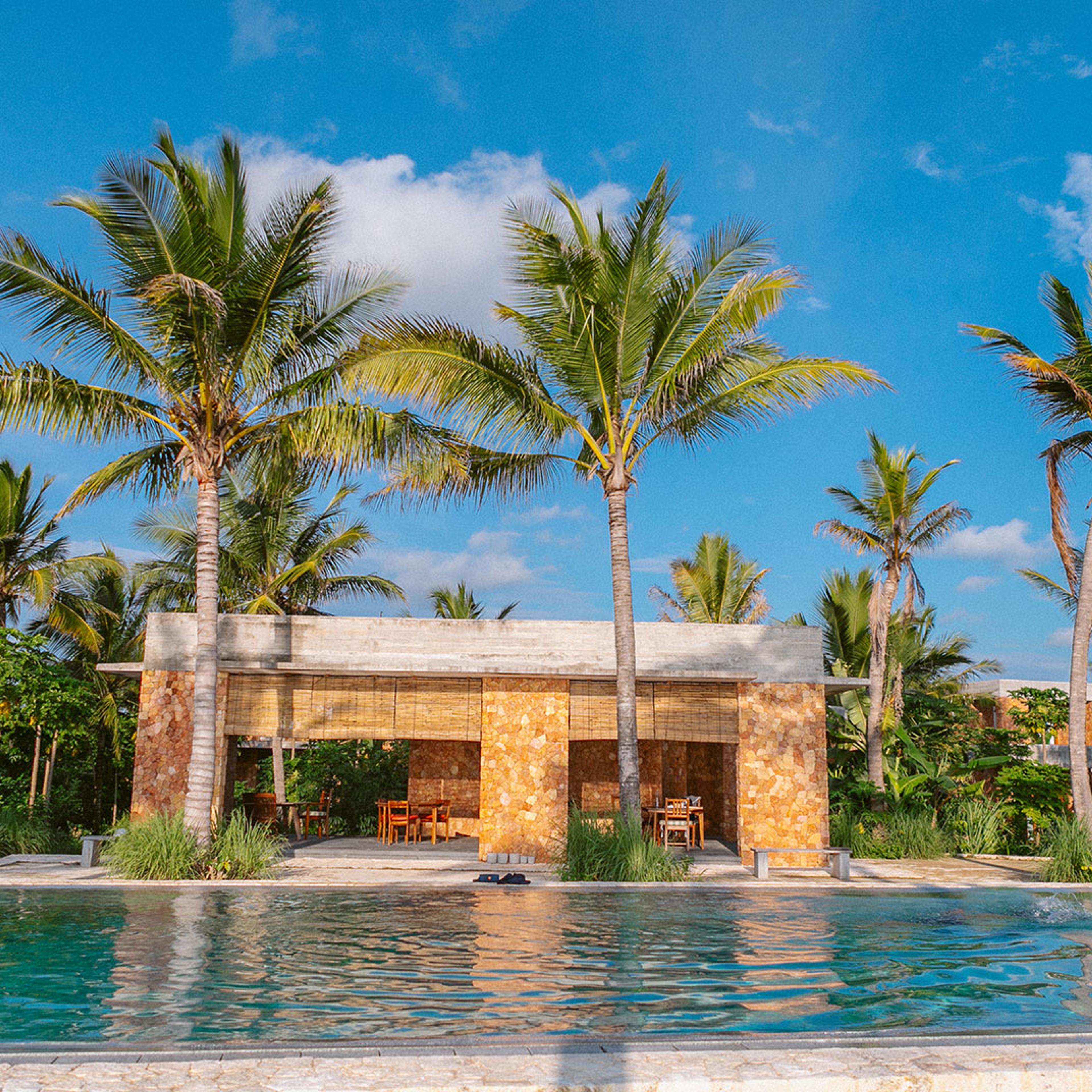 A coral-stone building among palms beside the pool