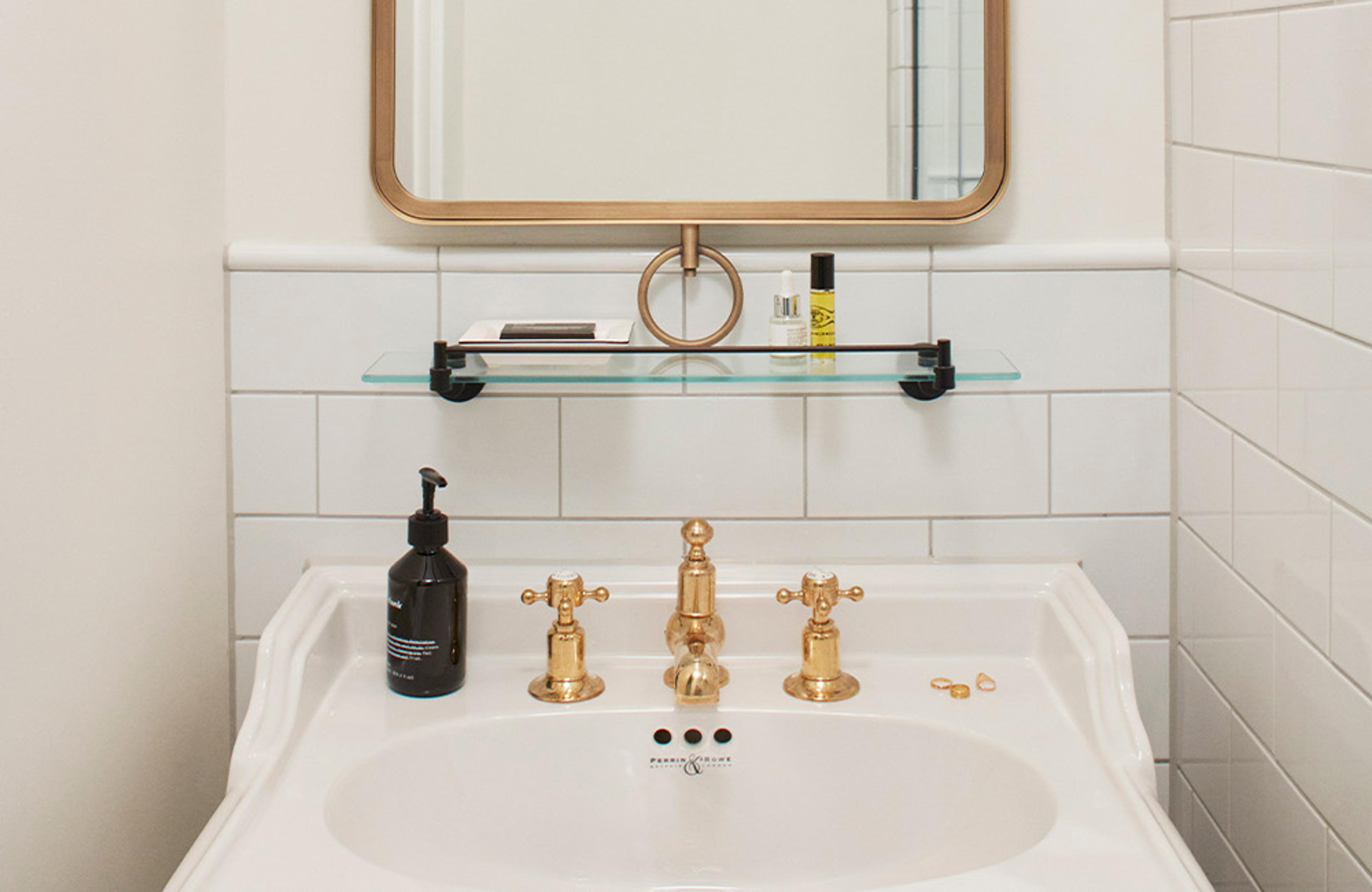 A white pedestal basin with brass taps under a round brass-framed mirror.