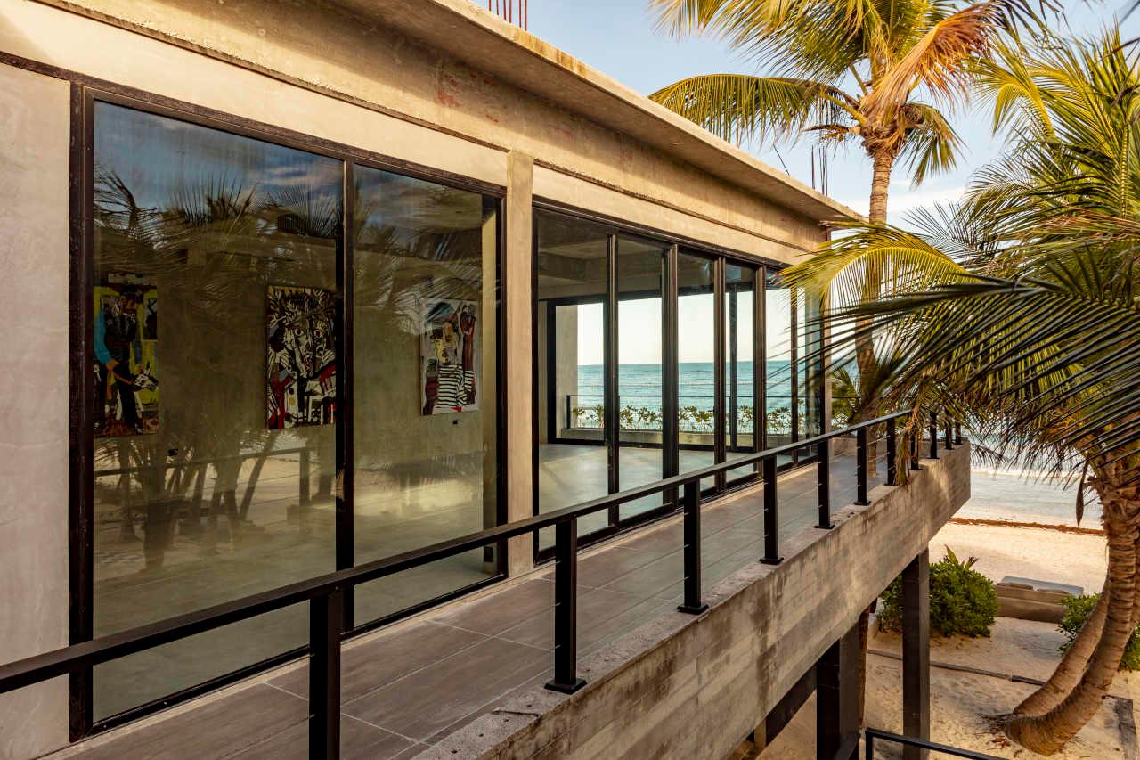 A concrete balcony walkway along a glass-walled building, with palm trees and the sea beyond.