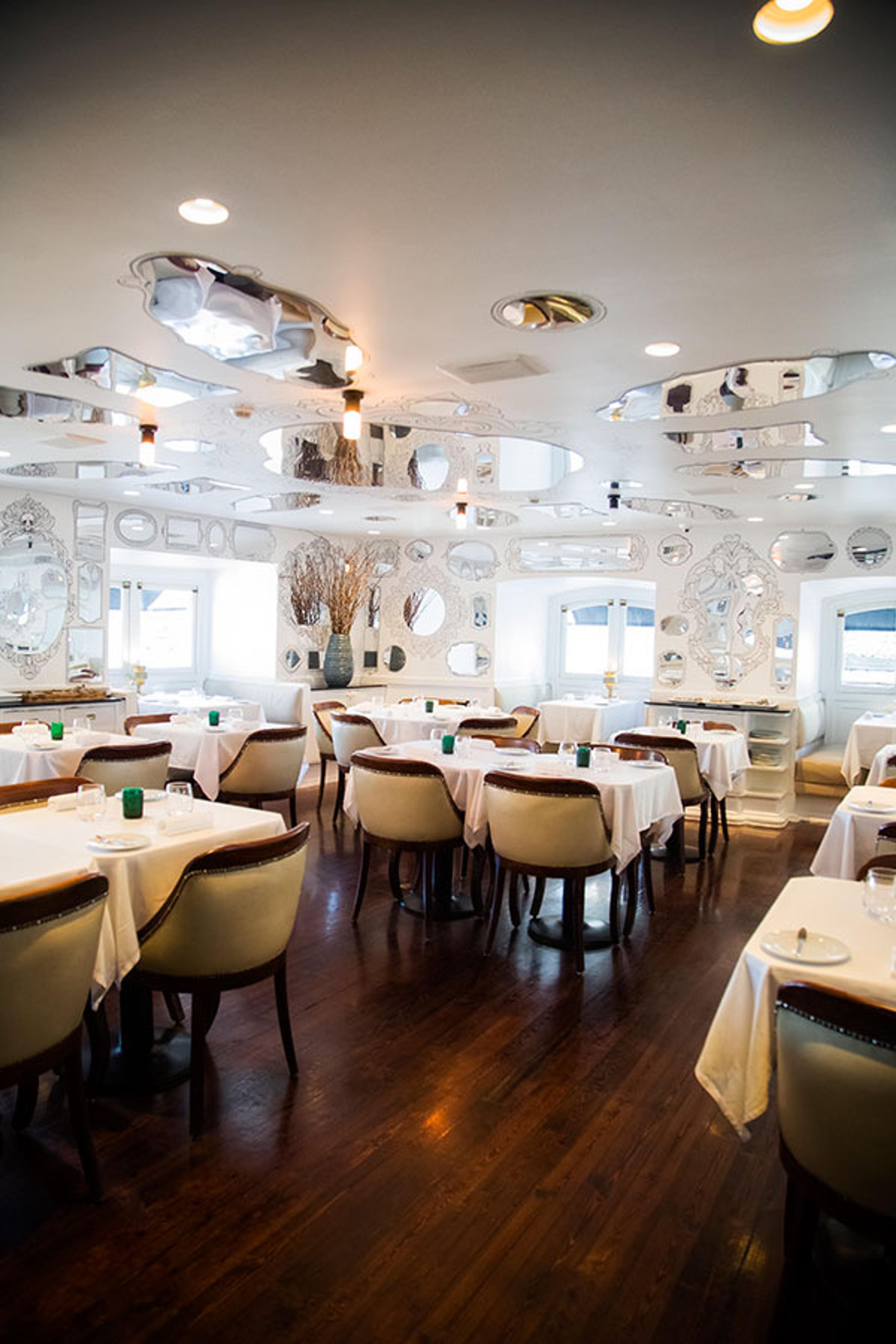 A white dining room hung with round mirrors, its tables laid with white cloths