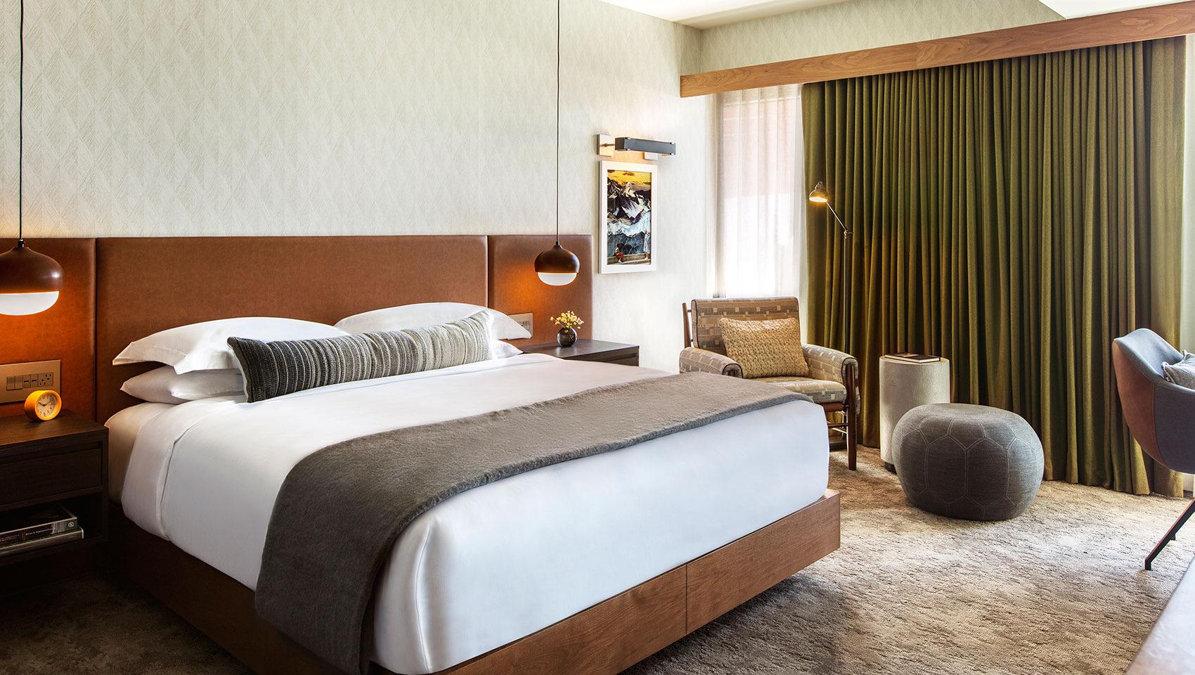 A king bed with white linens and a striped pillow, flanked by two round pendant lights and dark wood nightstands.