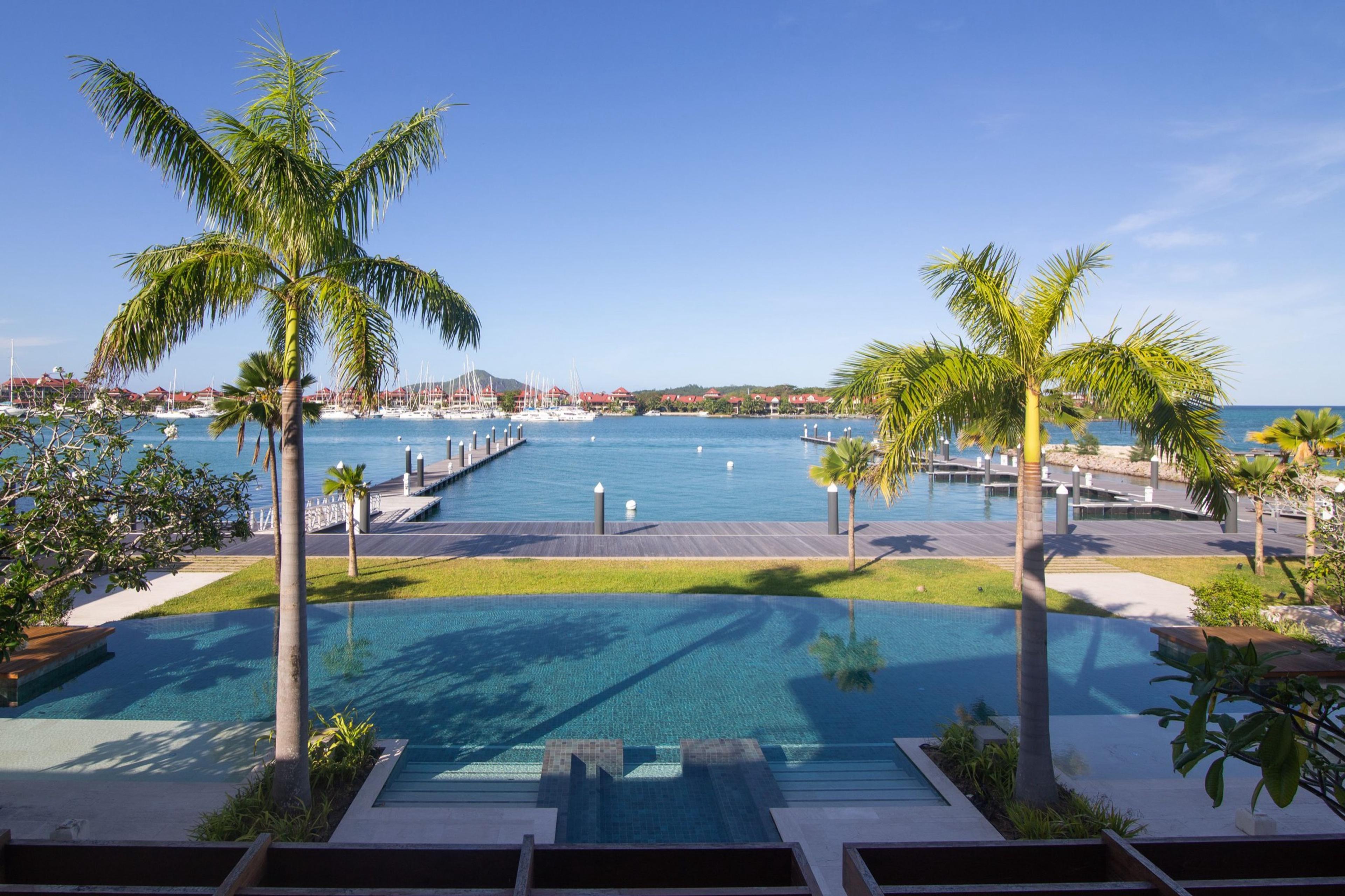 An infinity pool framed by two palm trees, looking out over a marina full of moored yachts.