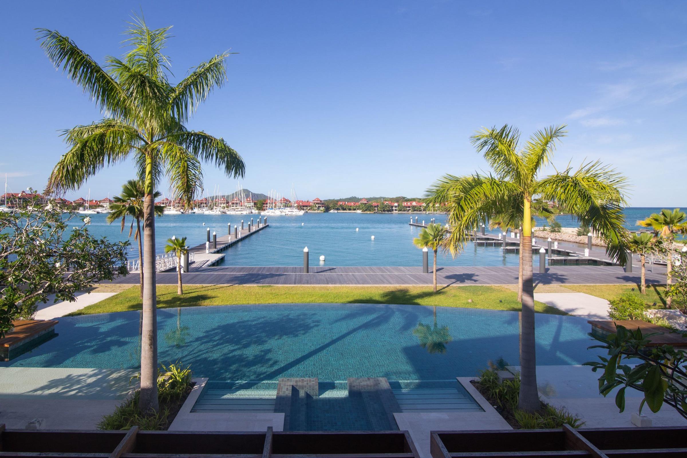 An infinity pool framed by two palm trees, looking out over a marina full of moored yachts.