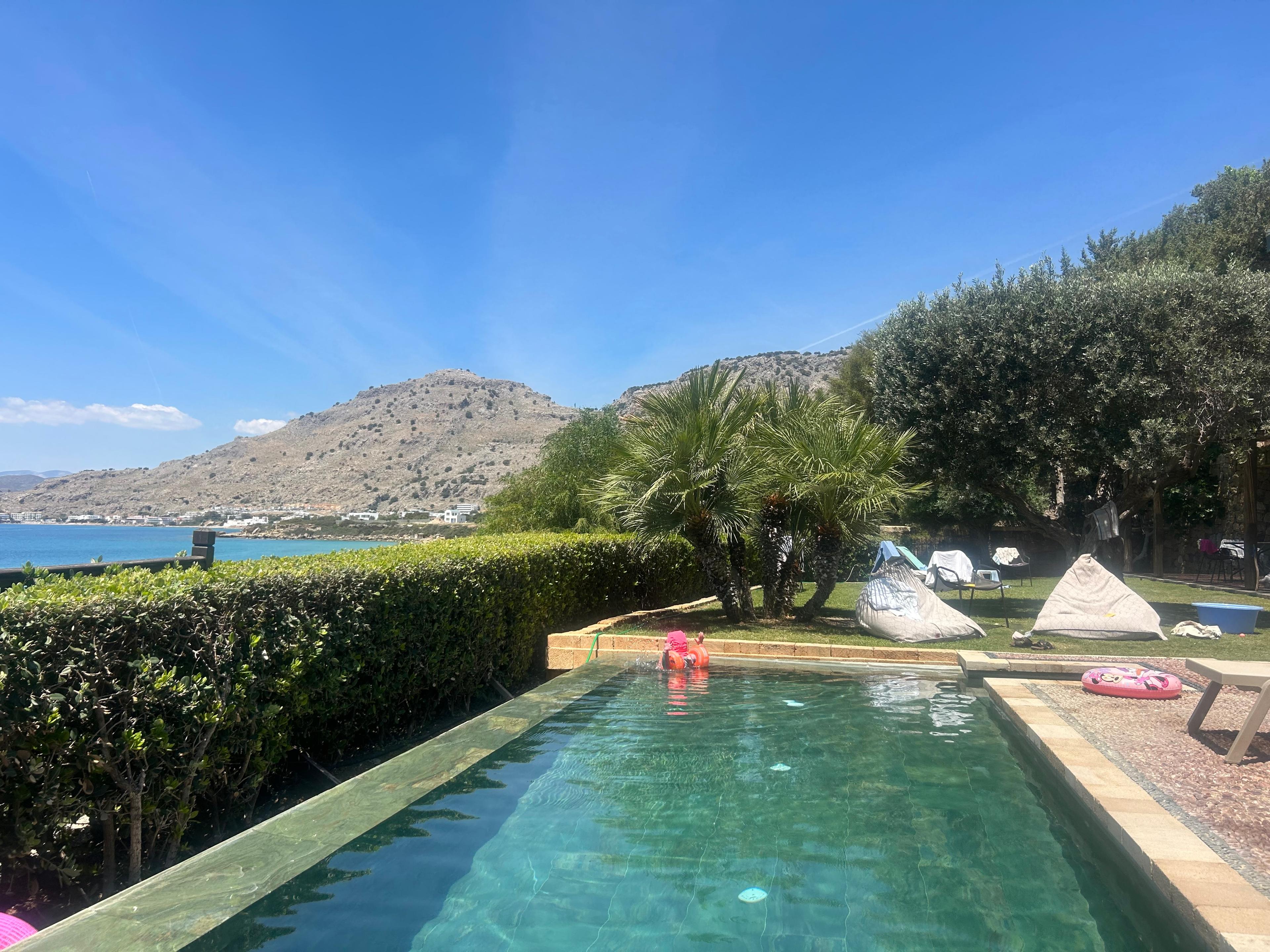 The pool's full length with sunbeds, palm trees and hills across the bay under a clear sky