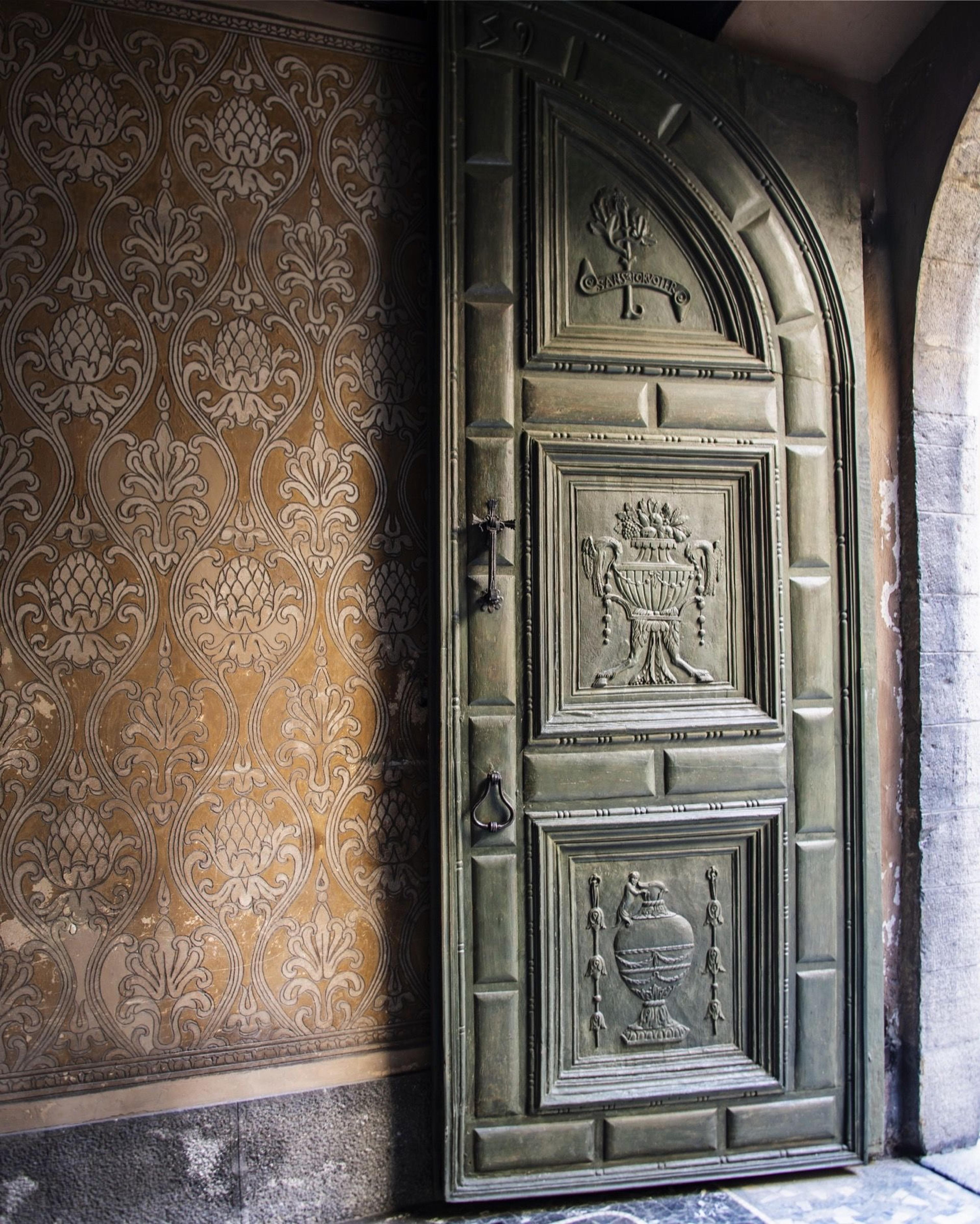 a large carved and painted antique door set in a stone archway, beside a wall of patterned gold damask