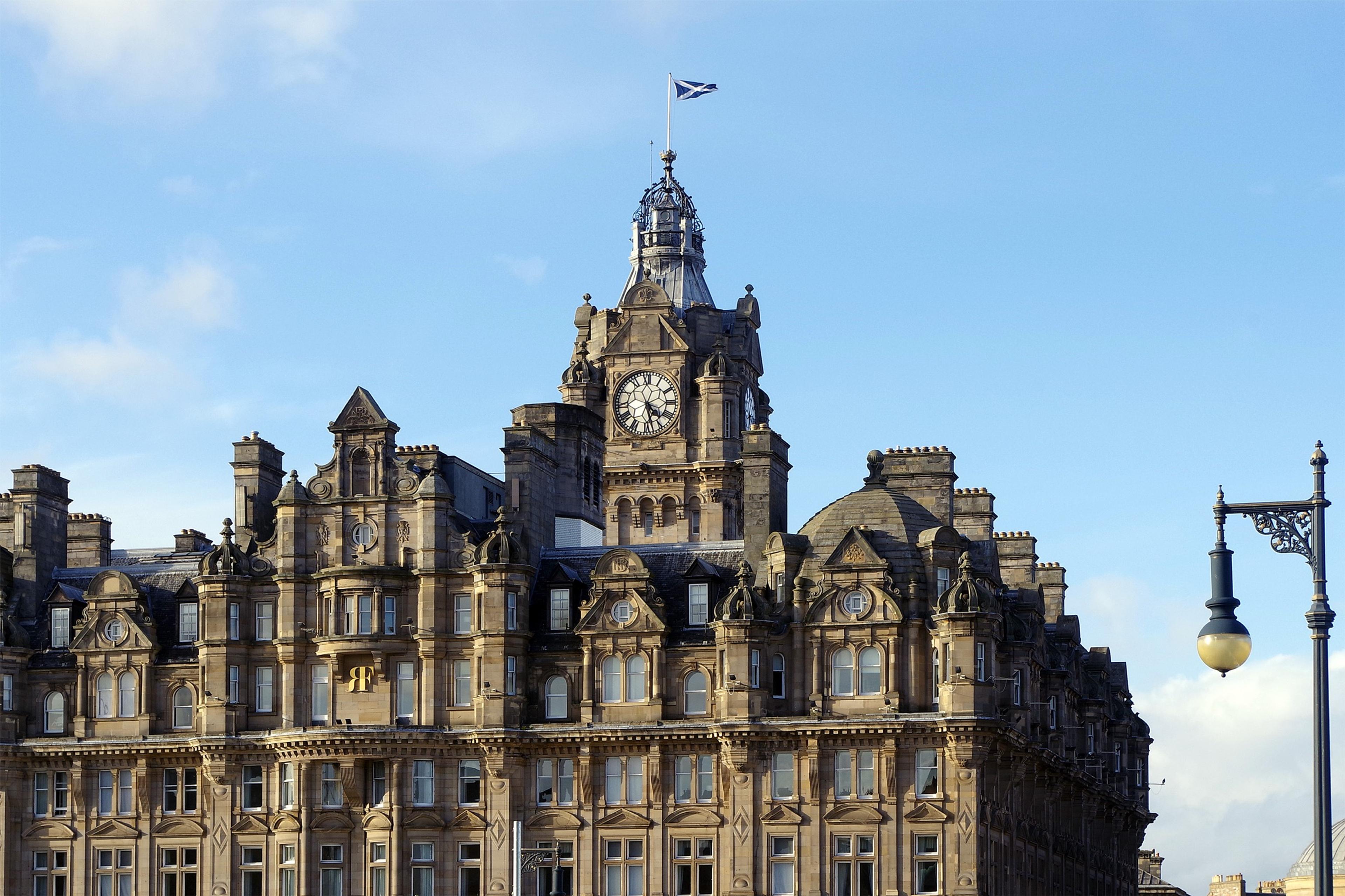 The Balmoral's sandstone front and clock tower at the east end of Princes Street, under a blue sky.