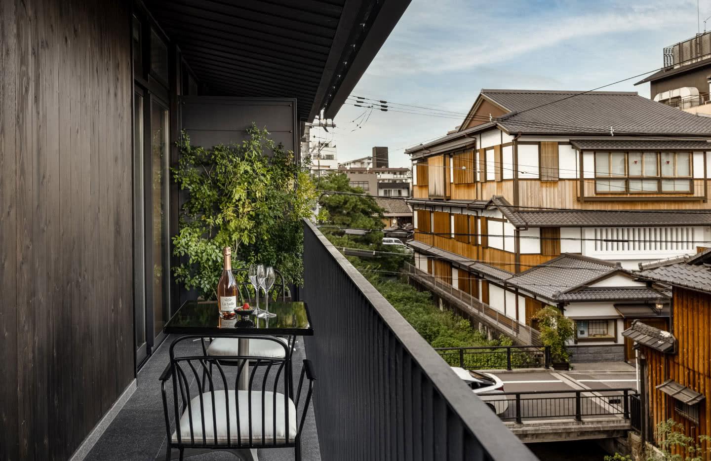 a small balcony table set with a bottle and two glasses, looking out over the tiled roofs of neighbouring machiya