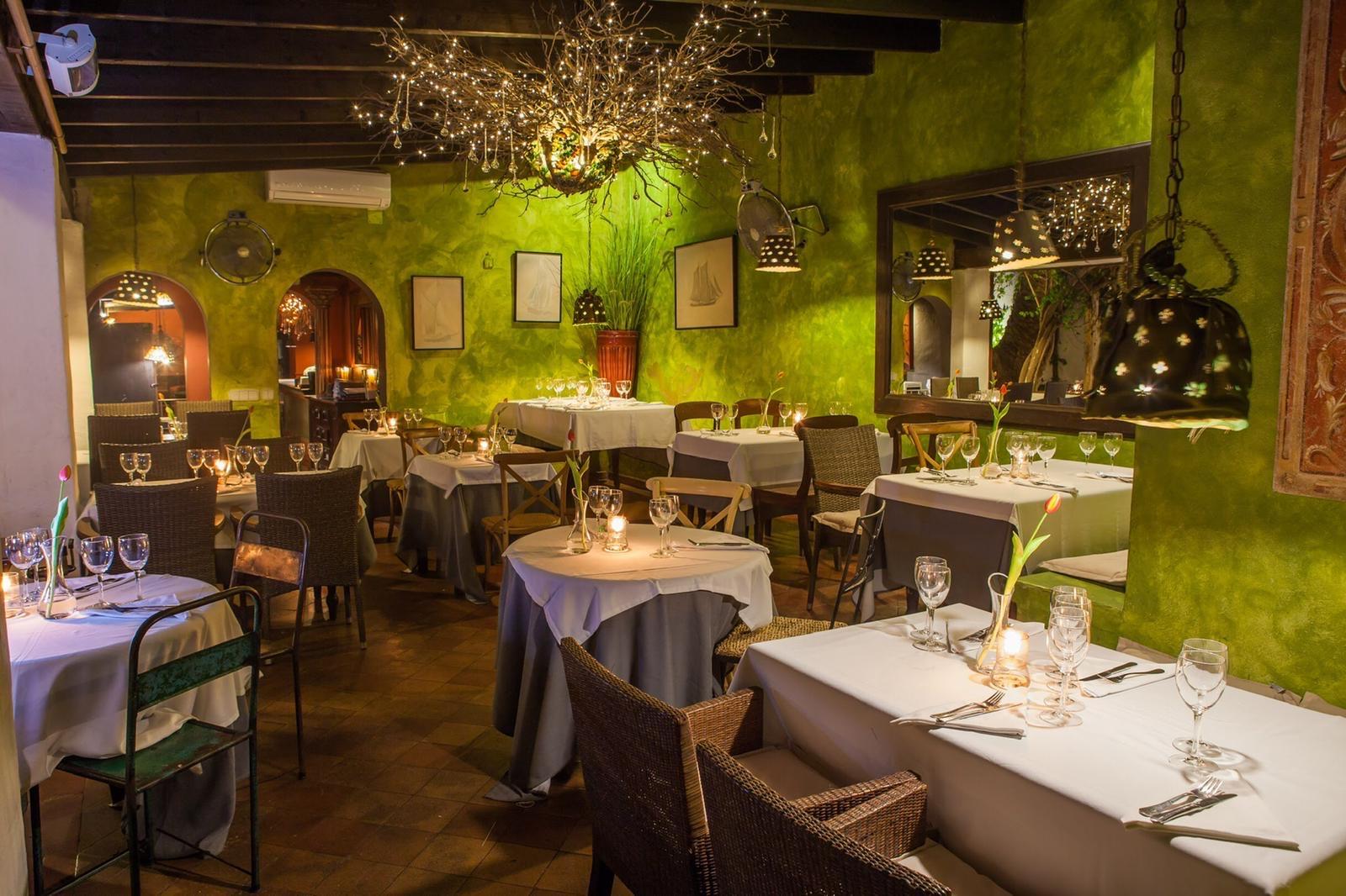 The dining room by candlelight: green walls, white tablecloths and a chandelier of branches and fairy lights