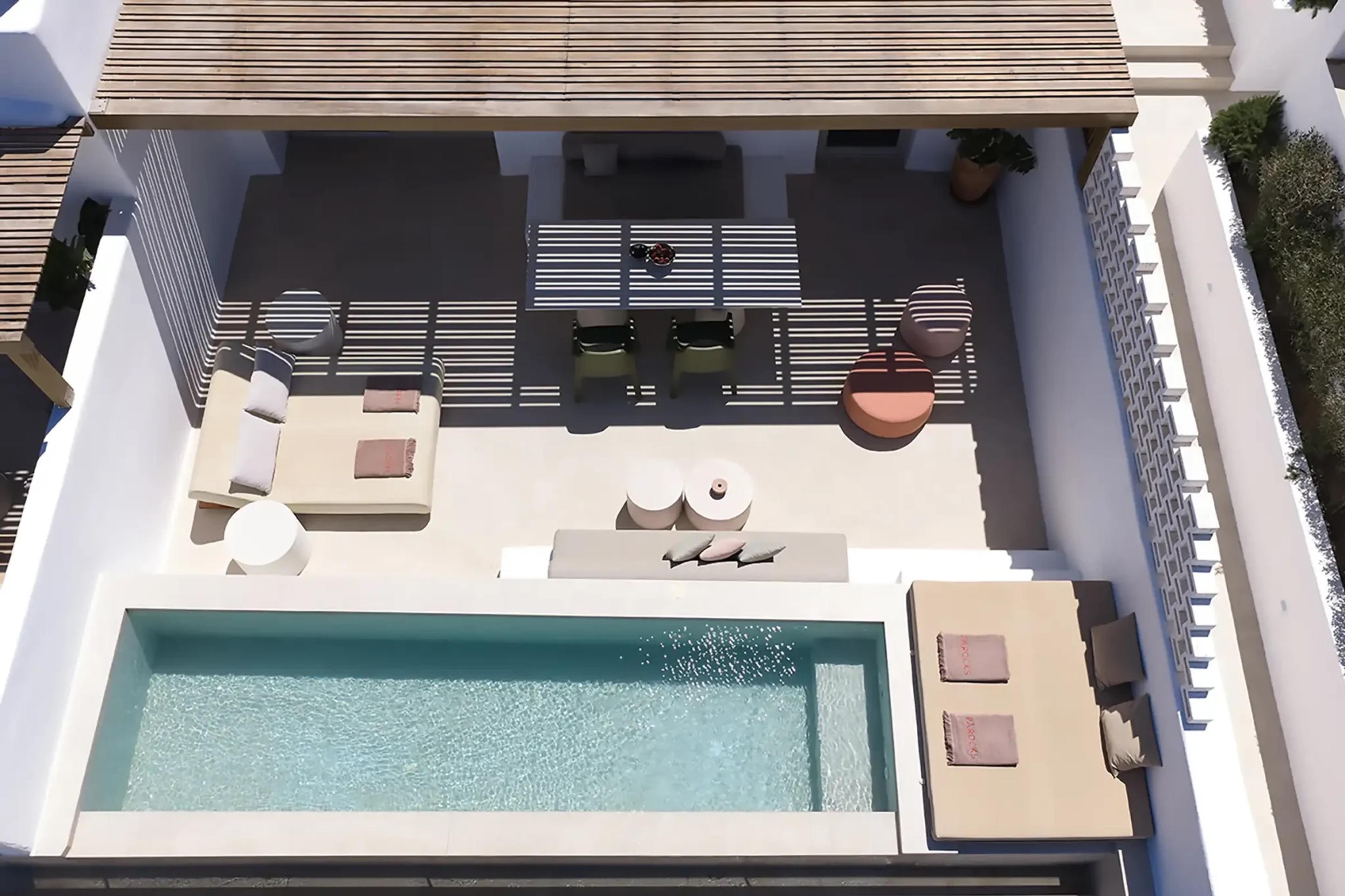An aerial view looking down into a narrow infinity-edged plunge pool on a private terrace with a pergola, sunbeds and a dining table.
