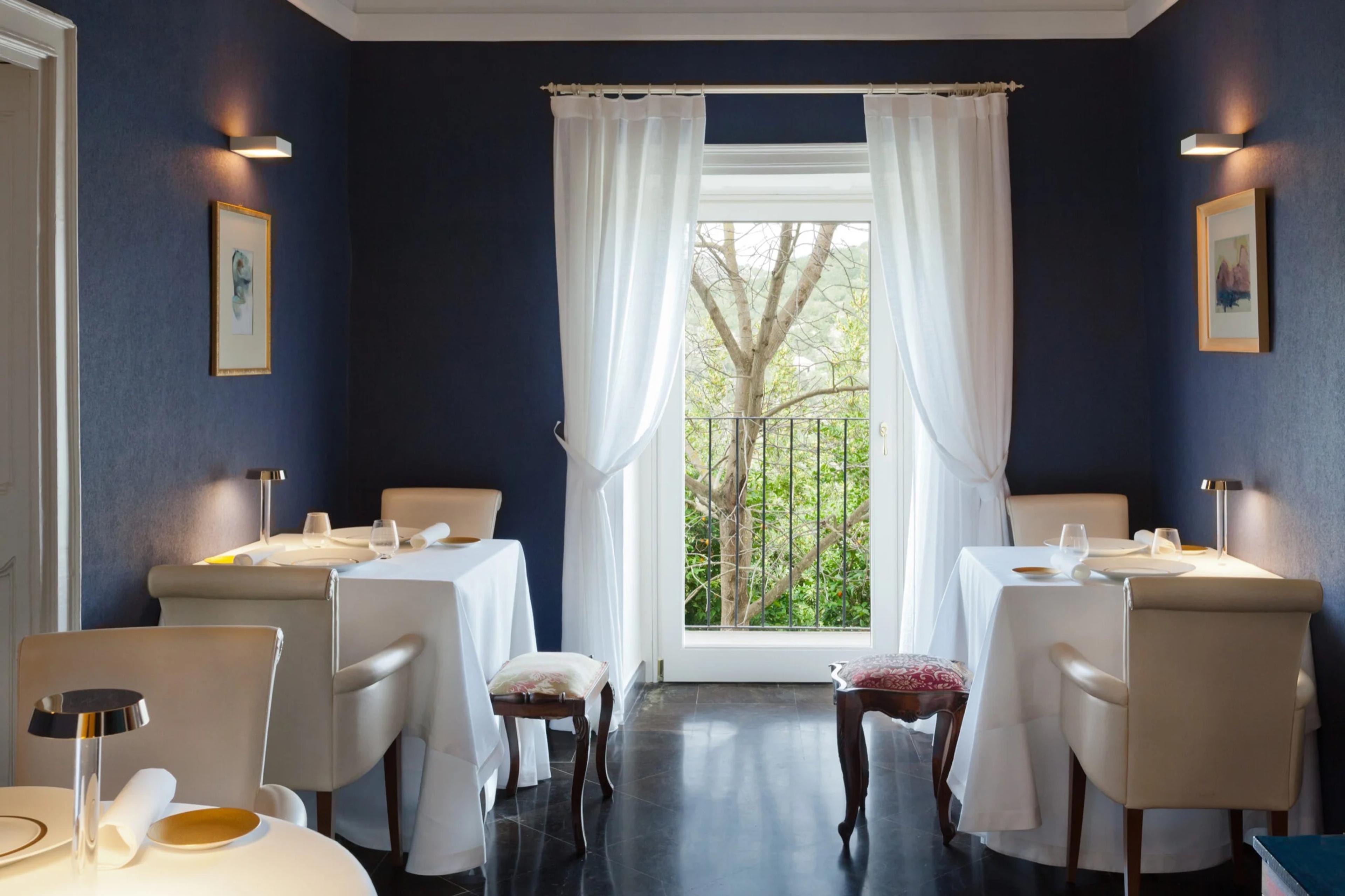 Duomo's dining room in Ragusa Ibla, white-clothed tables against deep blue walls and a tall curtained window