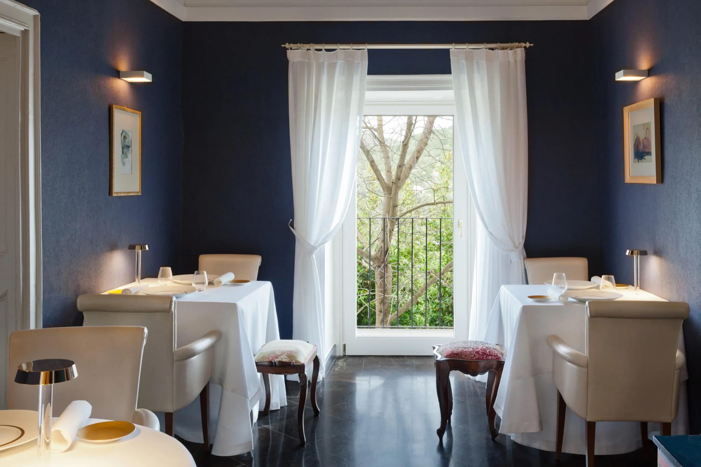 Duomo's dining room in Ragusa Ibla, white-clothed tables against deep blue walls and a tall curtained window