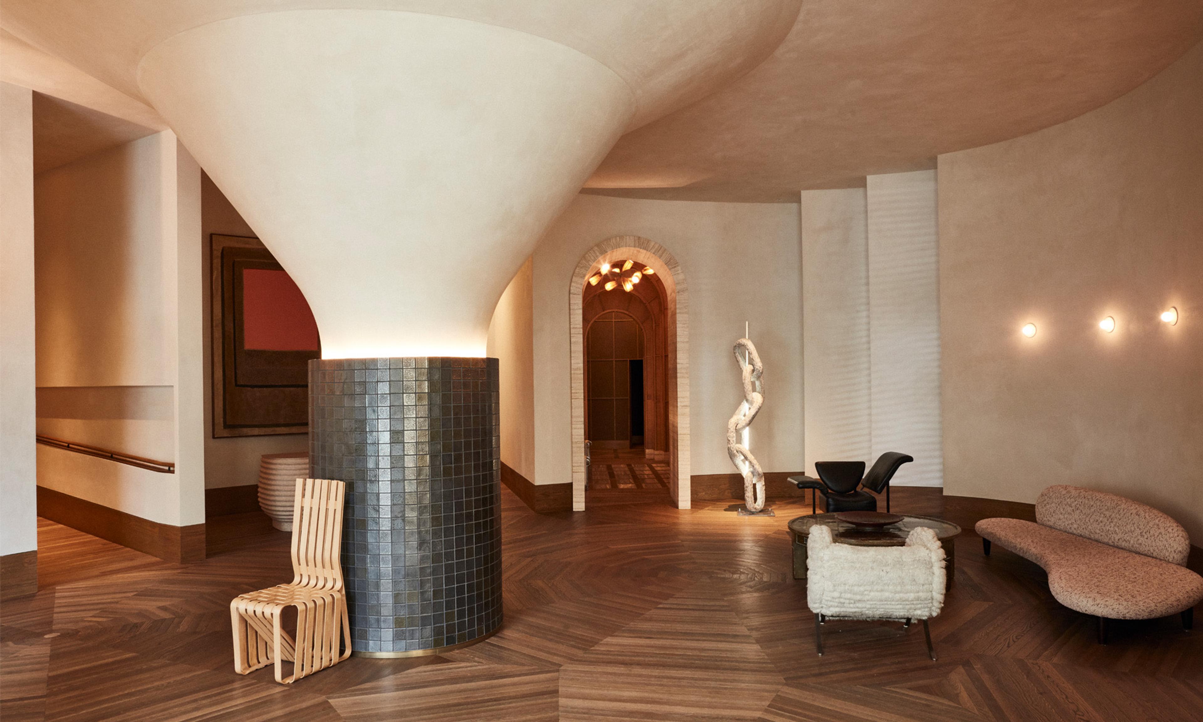 A hotel lobby with a sweeping cone-shaped plaster ceiling over a tiled column, a wooden chair, and an arched doorway beyond.