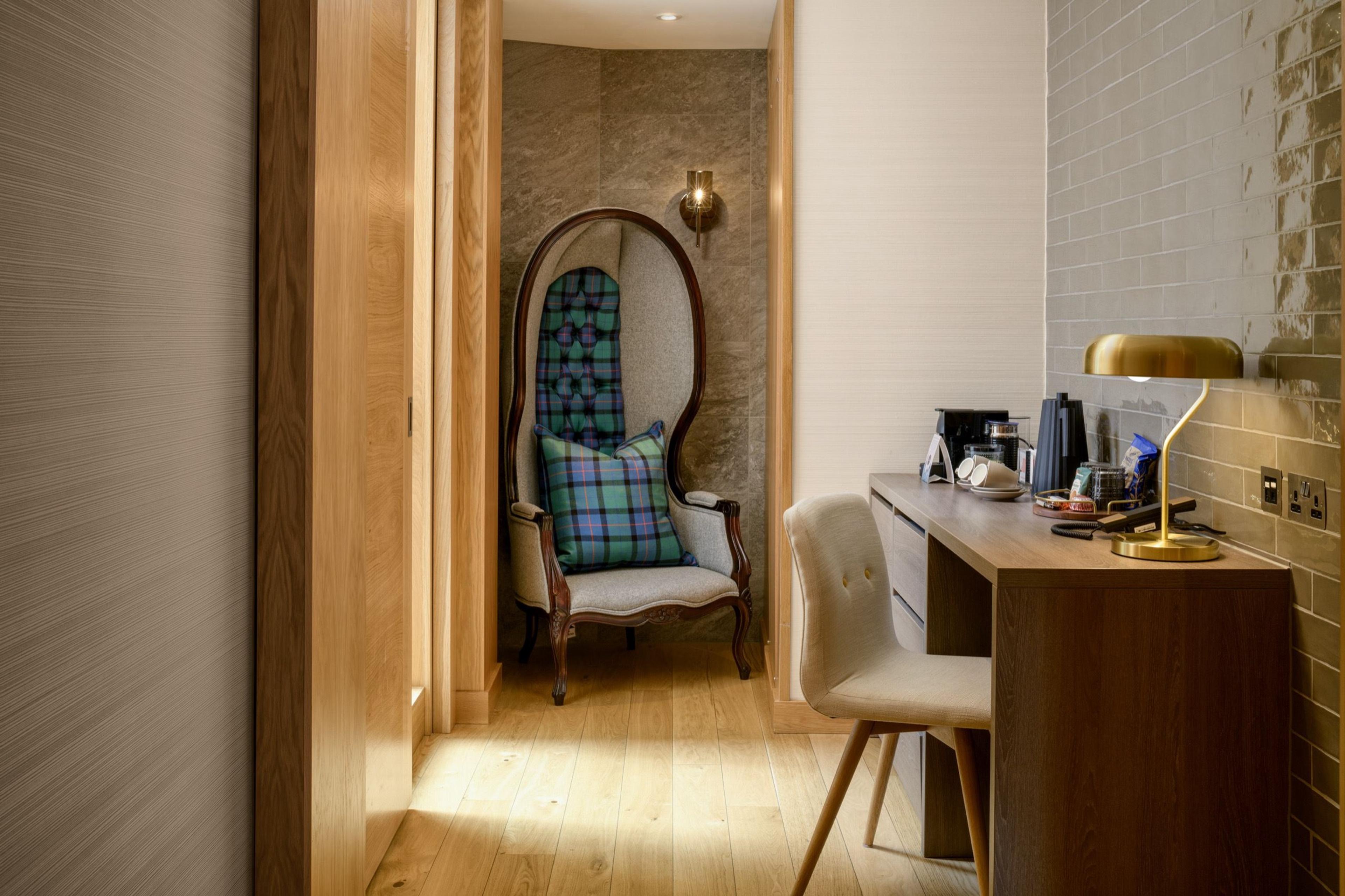 A wood-panelled hallway leading to a high-backed chair with a tartan cushion, beside a writing desk with a brass lamp.