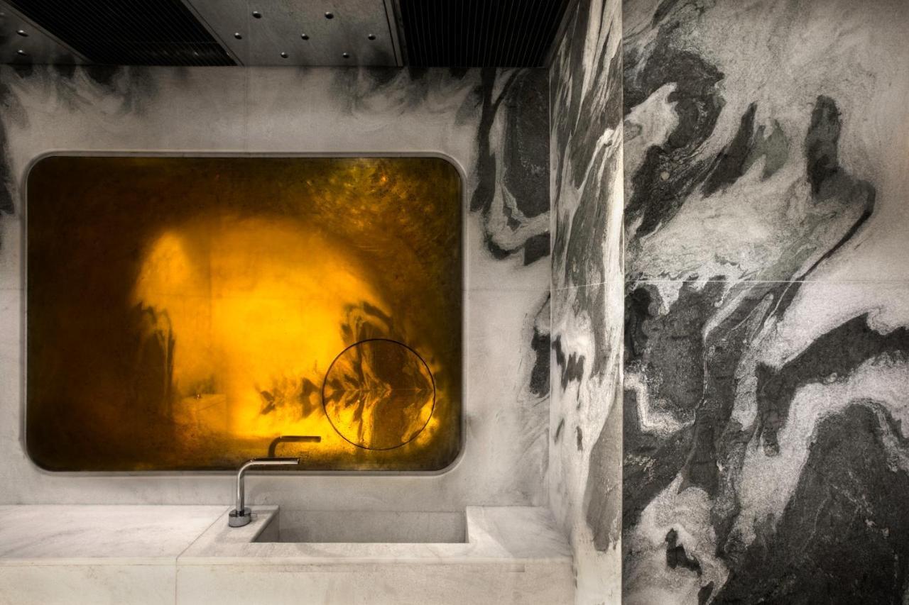 A concrete sink beneath an amber mirrored panel, next to a wall of dark marbling.