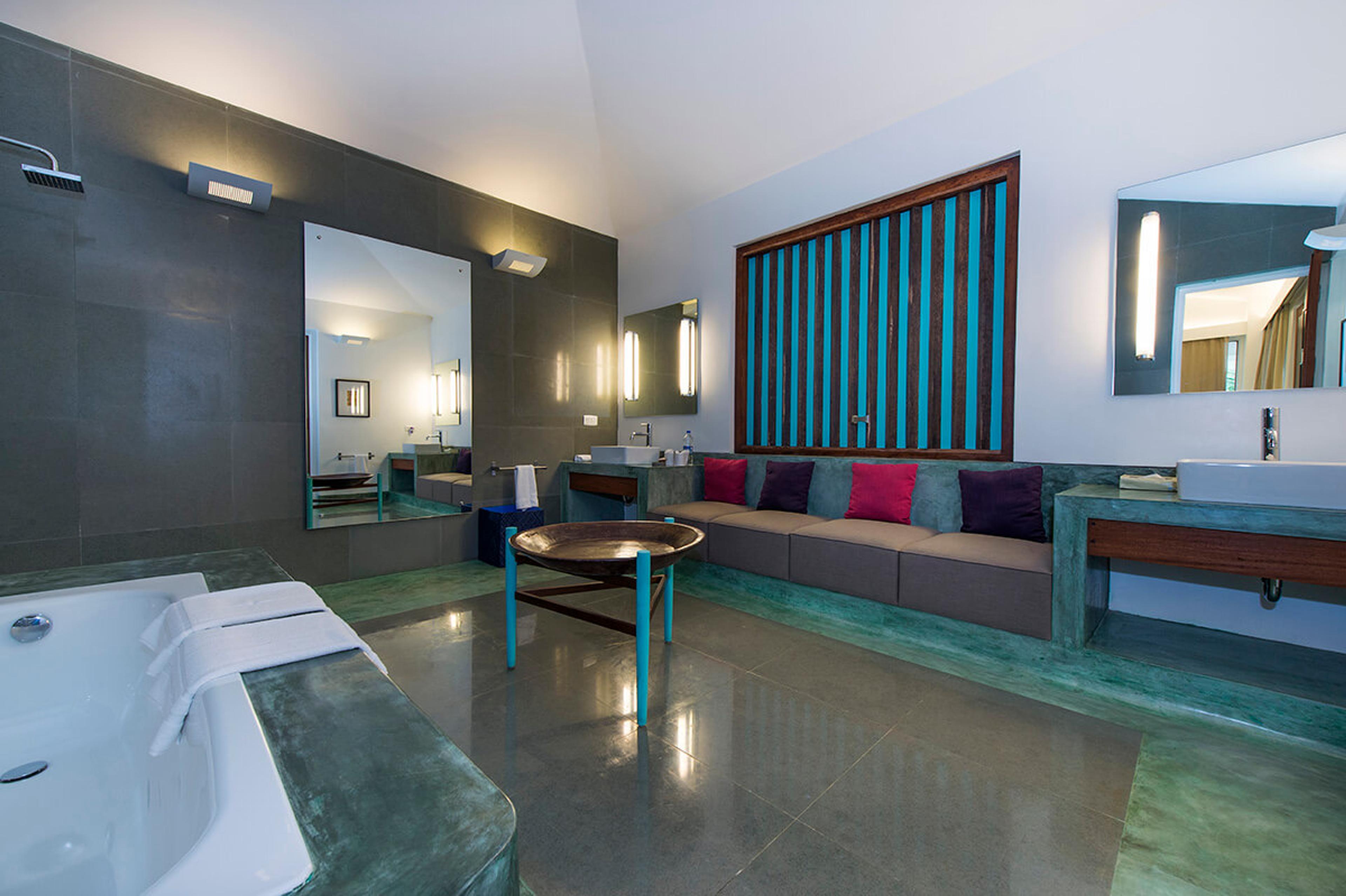 A bathroom with a freestanding tub, two mirrors and a bench seat, finished in green stone.