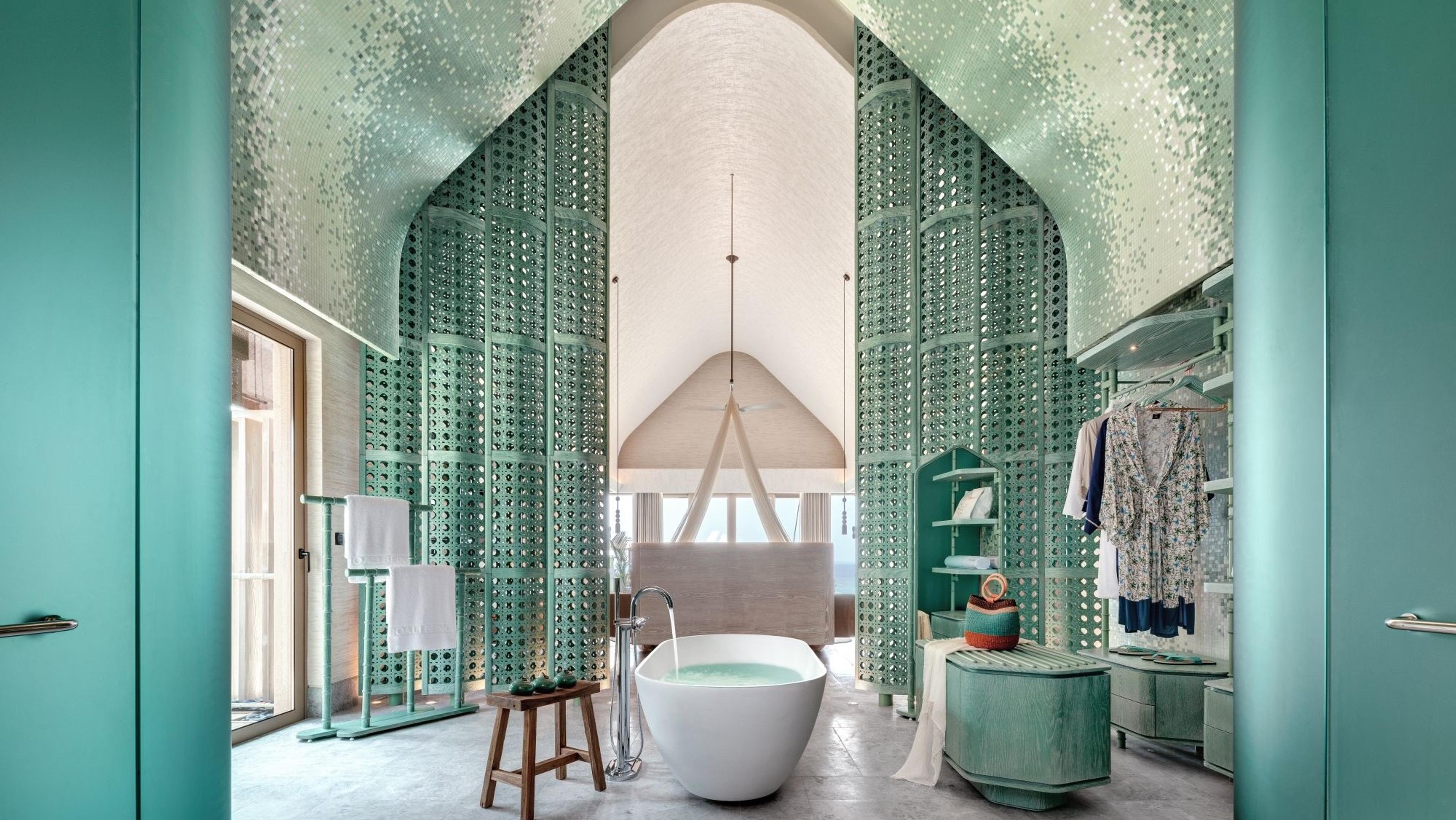 A bathroom with a freestanding bath between pale green carved screens under a peaked ceiling.