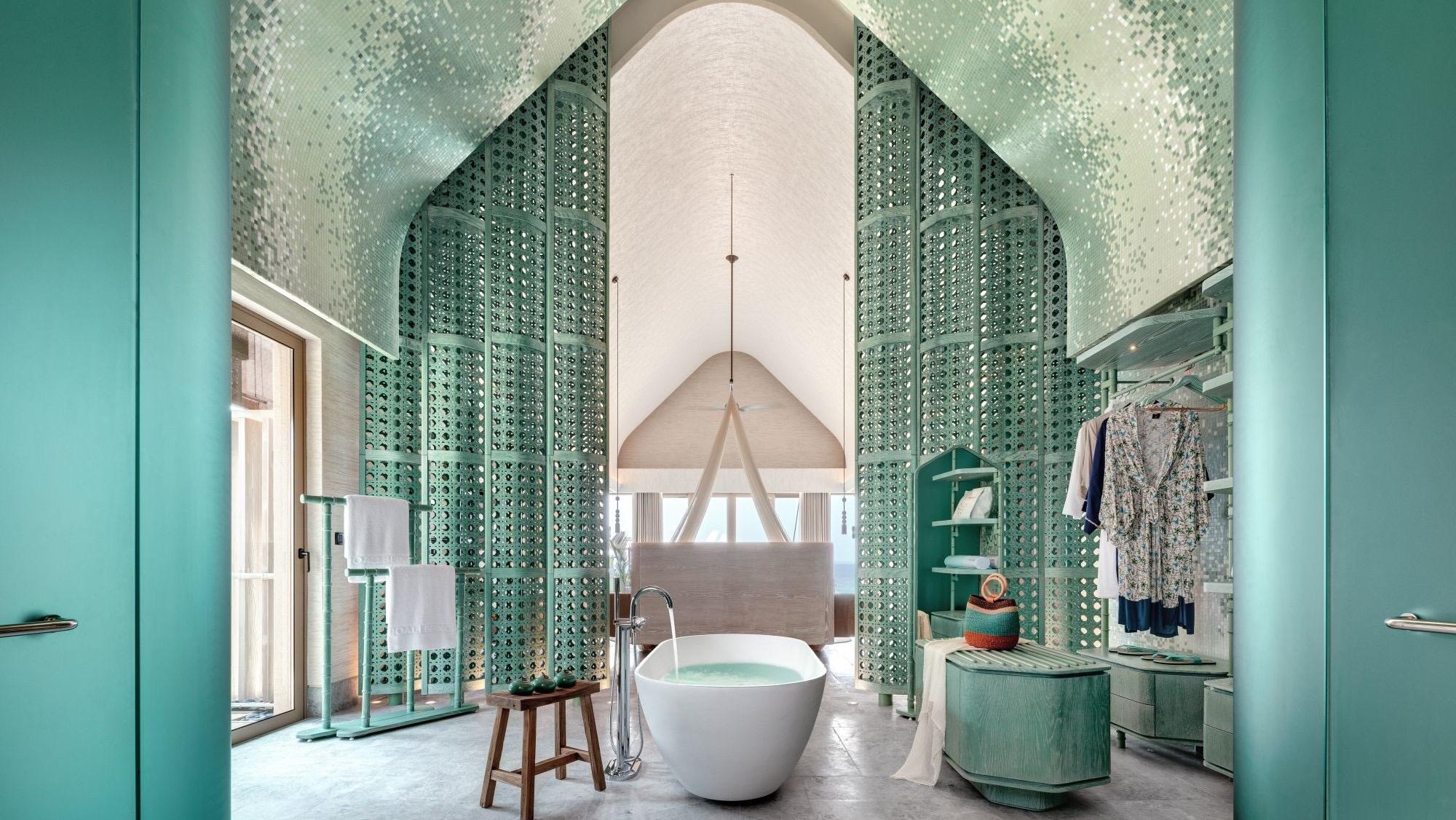 A bathroom with a freestanding bath between pale green carved screens under a peaked ceiling.