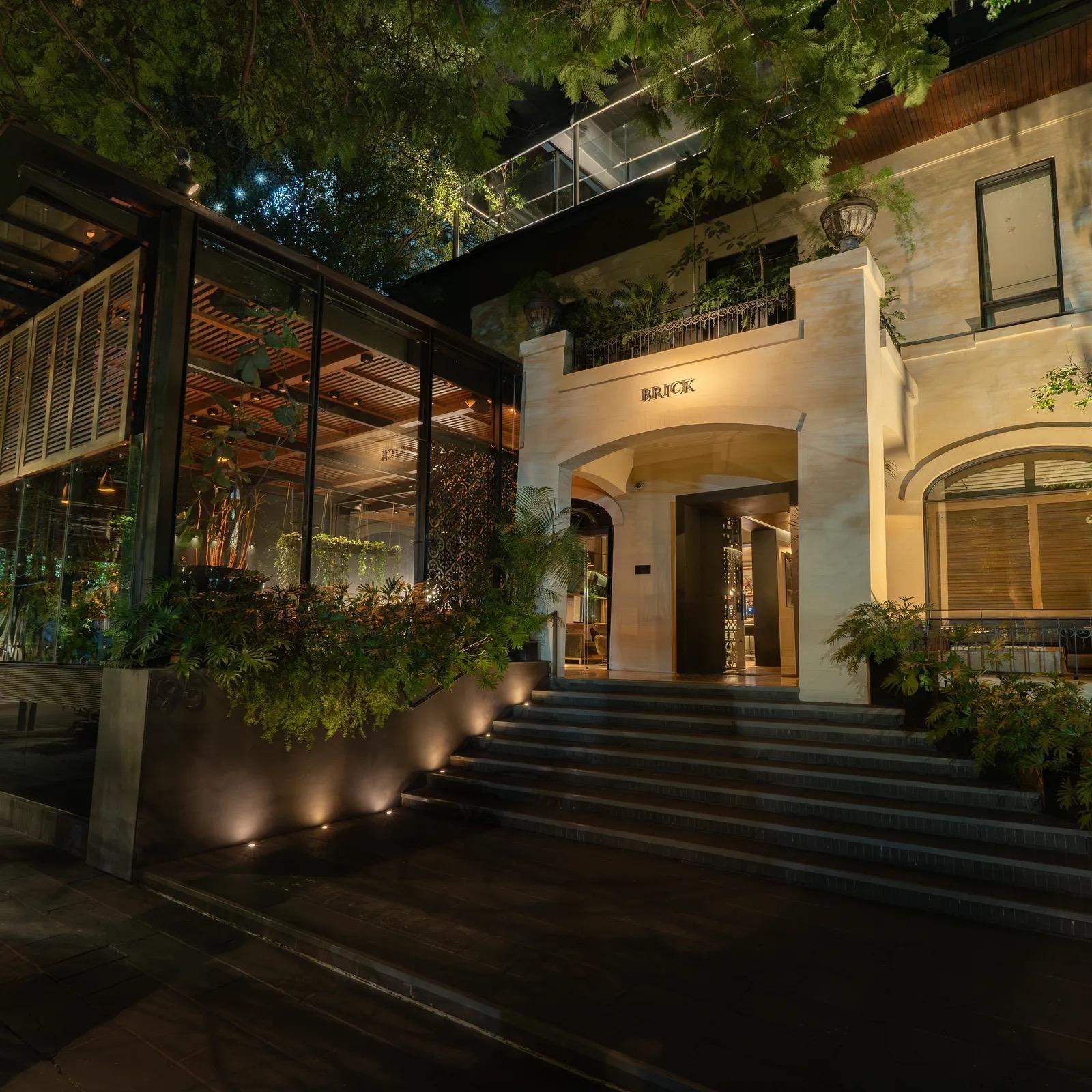 The hotel's lit entrance at night, with the BRICK sign over an arched doorway, a flight of steps and trees overhanging from above.