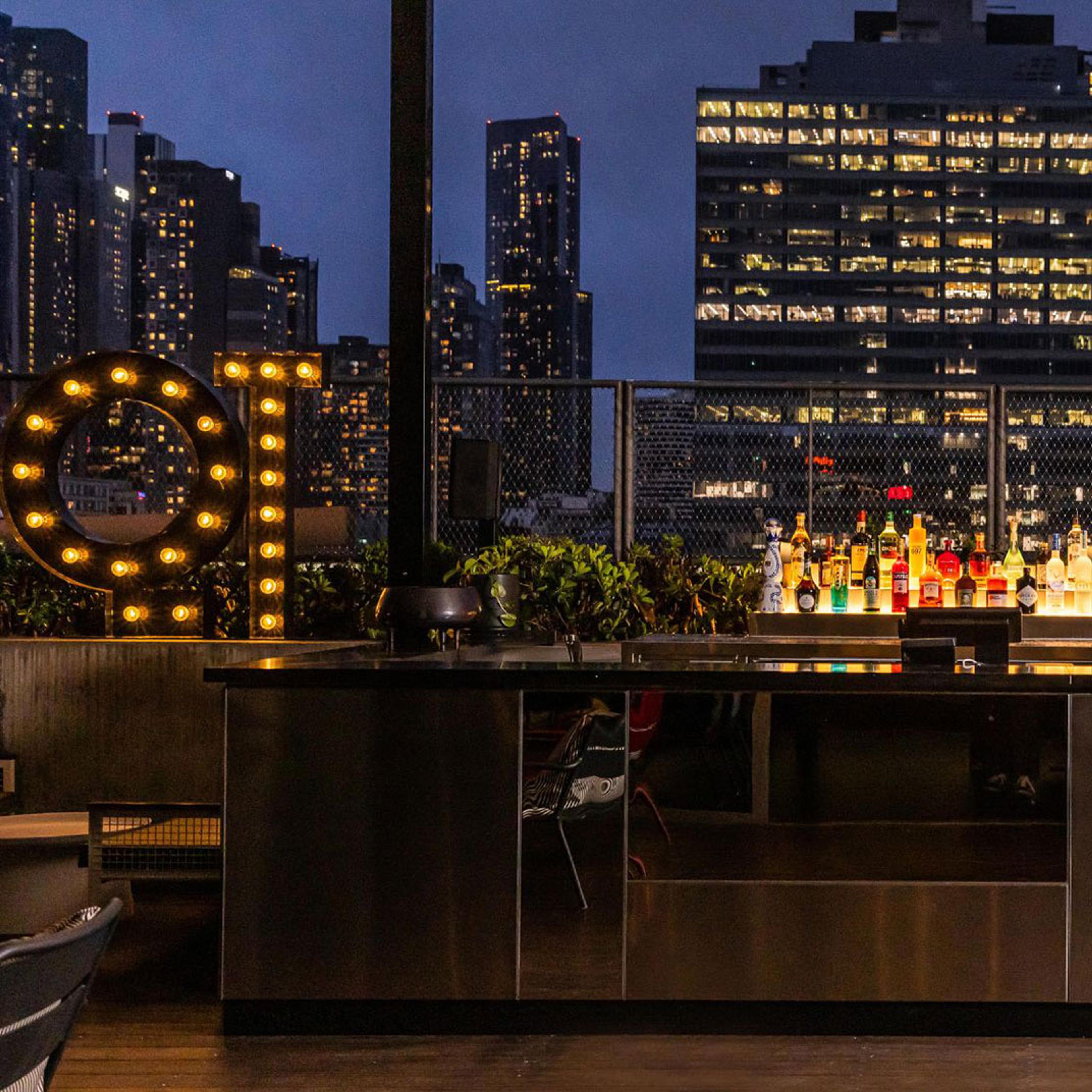 A rooftop bar at night among lit city towers