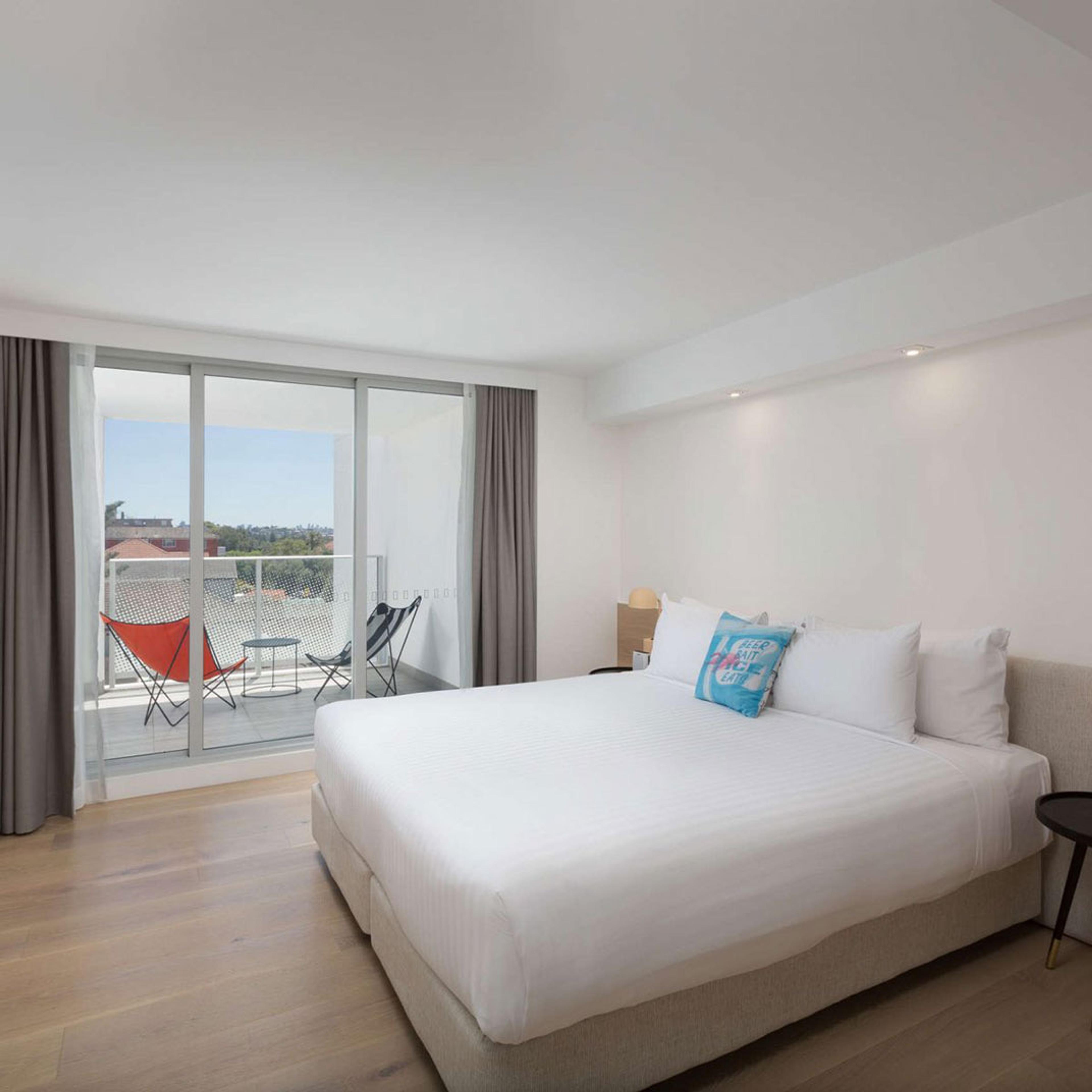 A bedroom with a white bed, blue cushions and a window onto the street