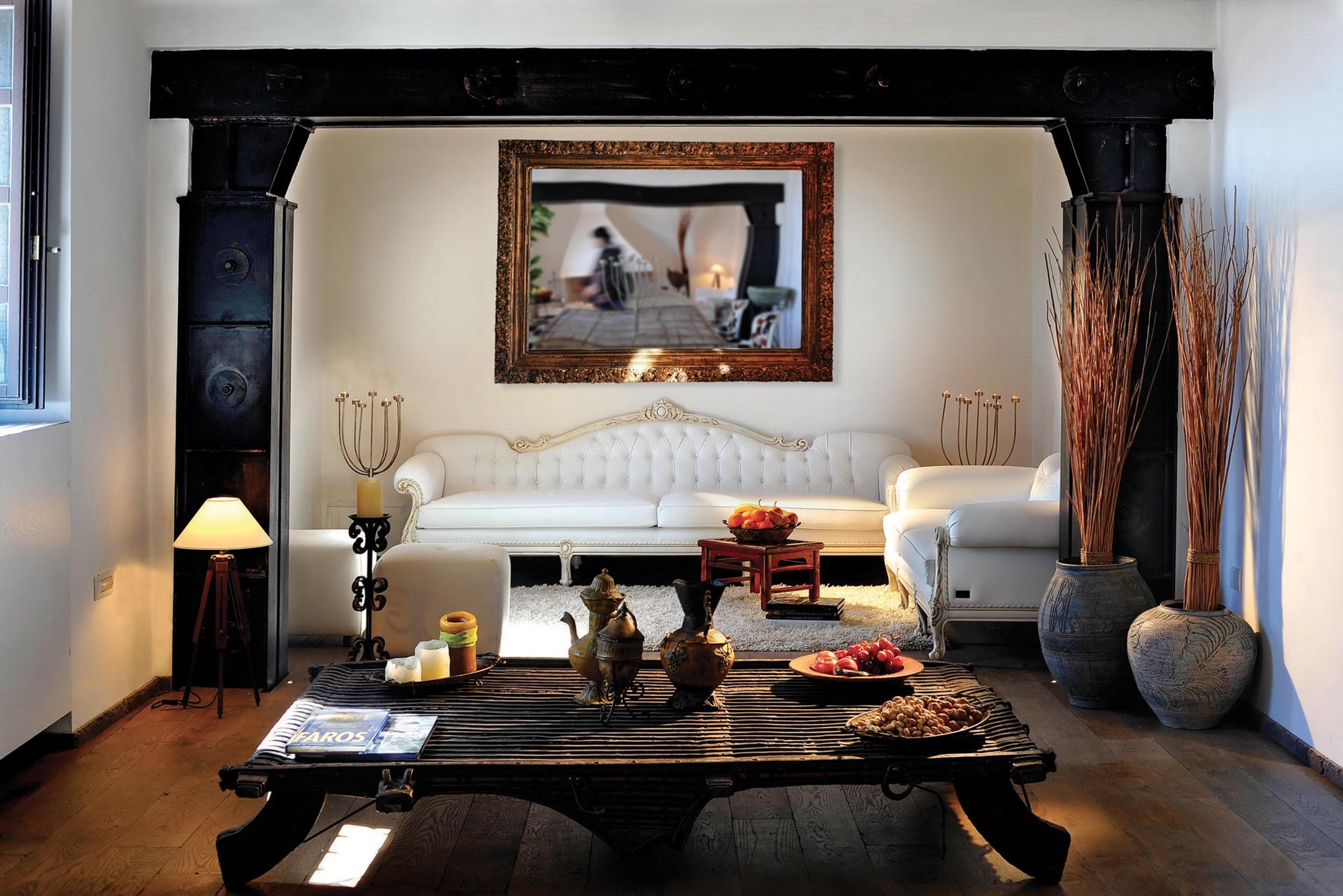 A suite with white sofas, a carved dark wood table and a framed picture above