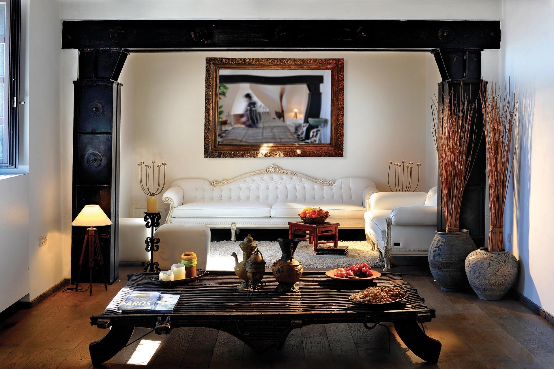 A suite with white sofas, a carved dark wood table and a framed picture above
