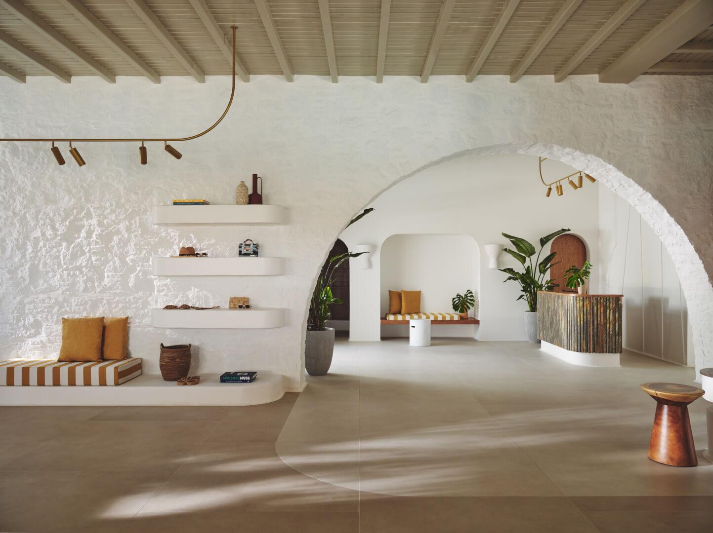 A hotel lobby with white arched doorways, built-in shelving holding books and ceramics, and striped cushioned benches.