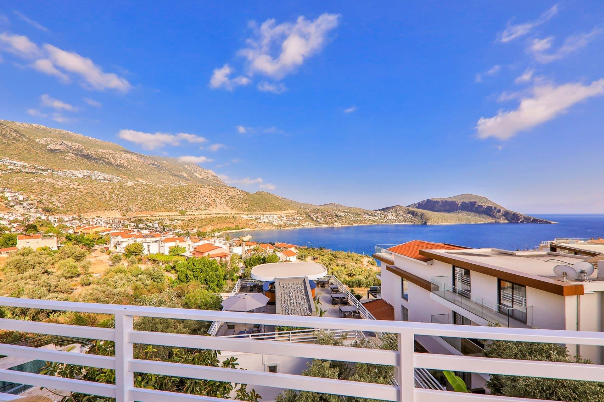 A view from a balcony railing over rooftops and a bay to hills beyond under a blue sky.
