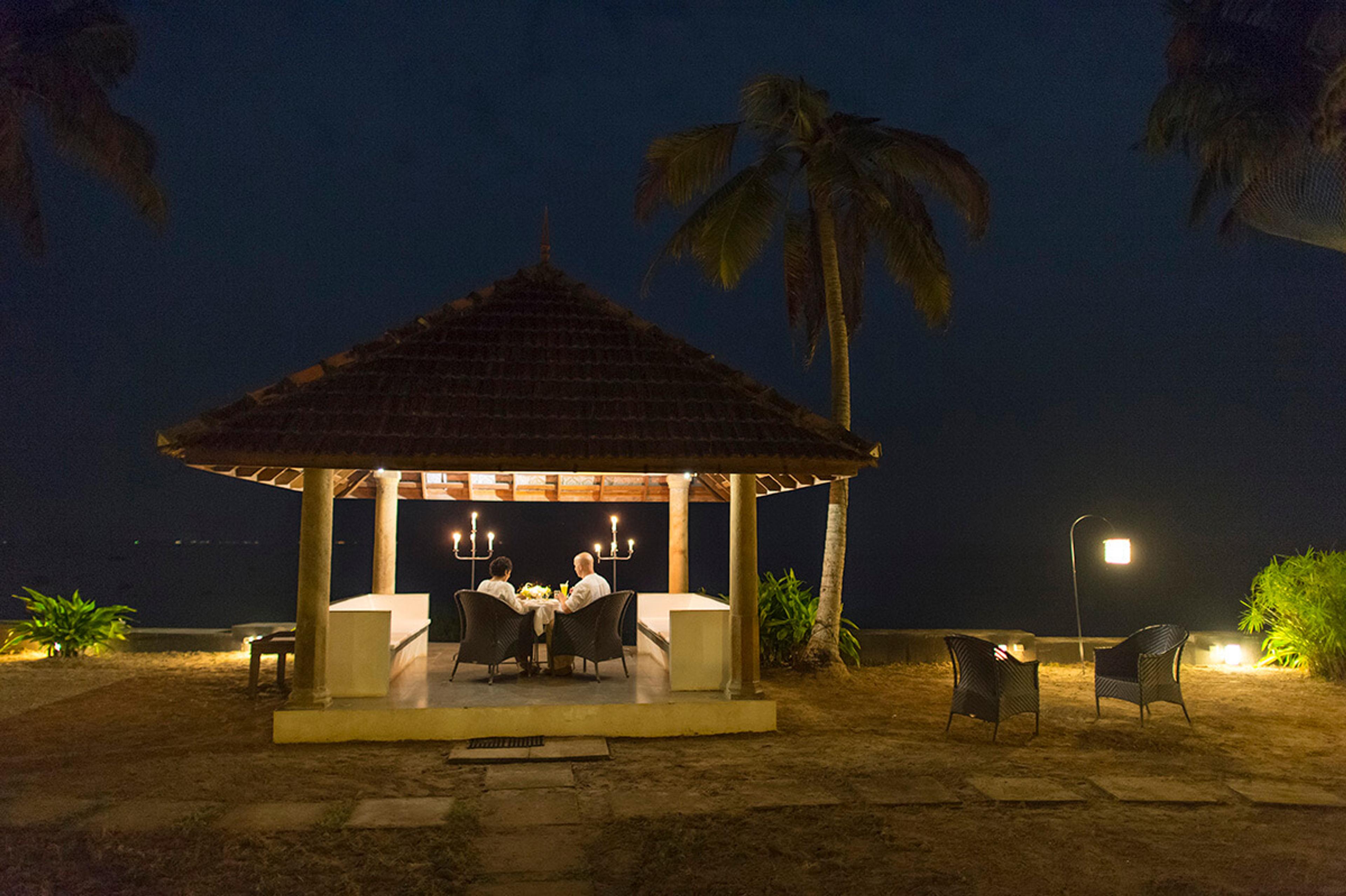 A candlelit table for two under a tiled pavilion by the water at night