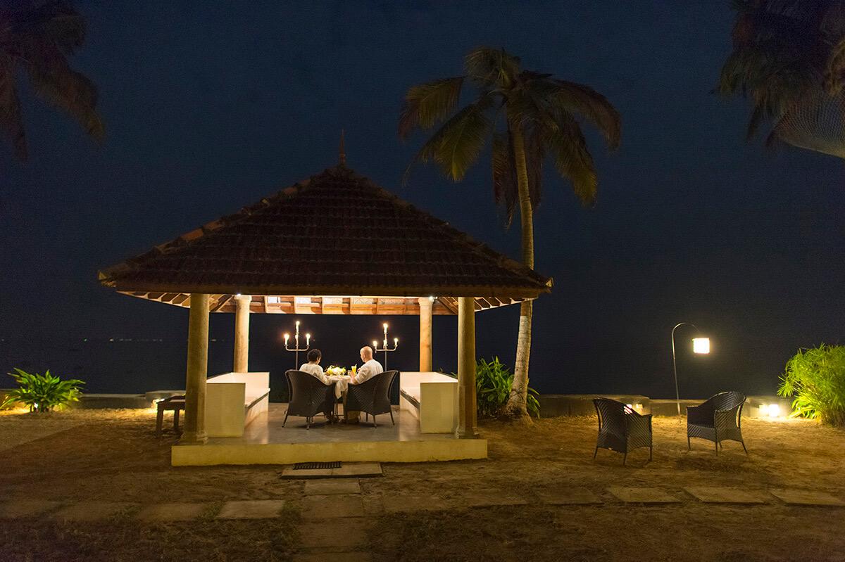 A candlelit table for two under a tiled pavilion by the water at night