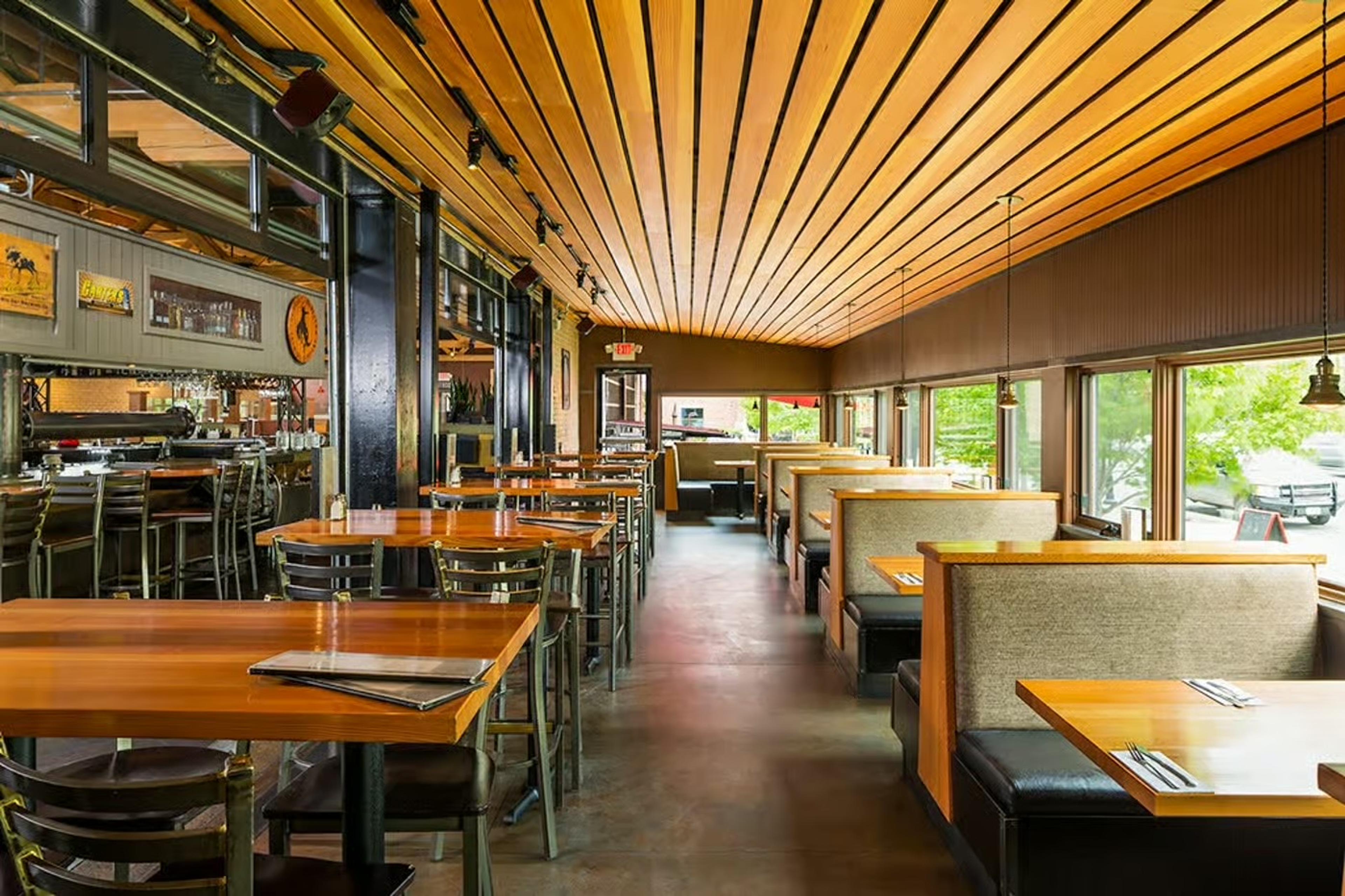 Wooden booths and long tables under a slatted timber ceiling, the bar along one side