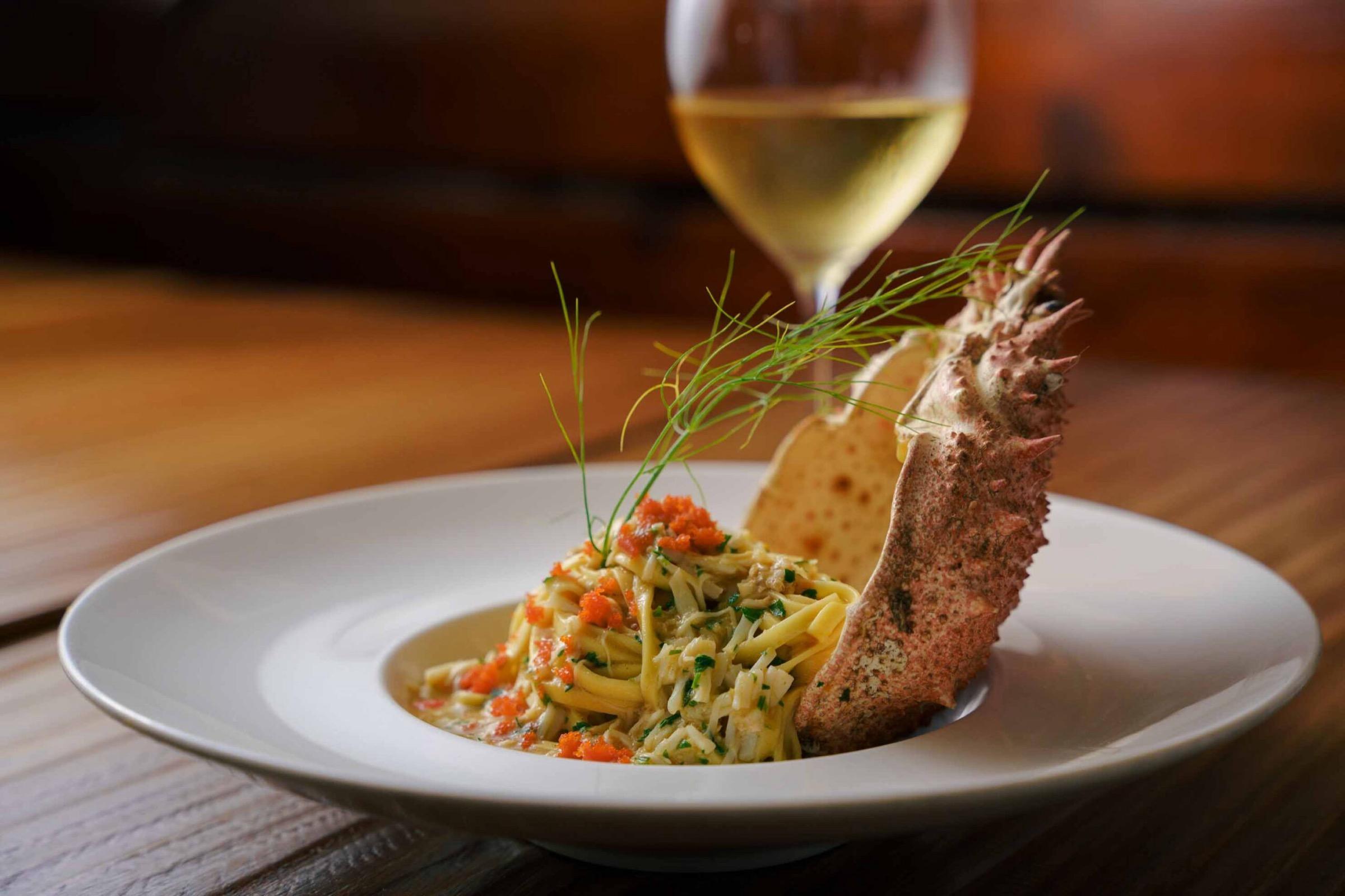 Pasta topped with a langoustine, a glass of white wine behind