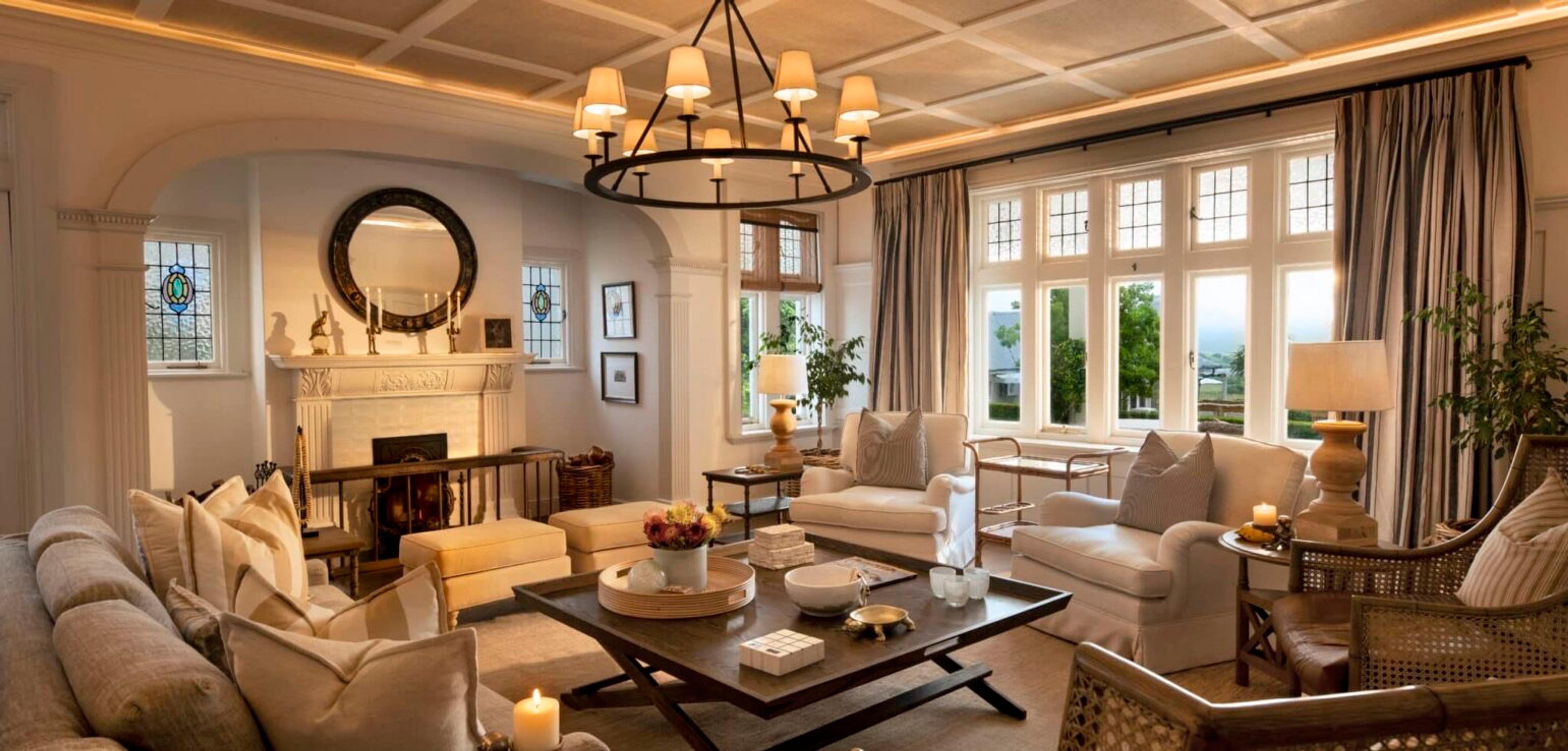 A living room with a fireplace, round mirror and stained glass windows, sofas arranged around a dark wood coffee table.