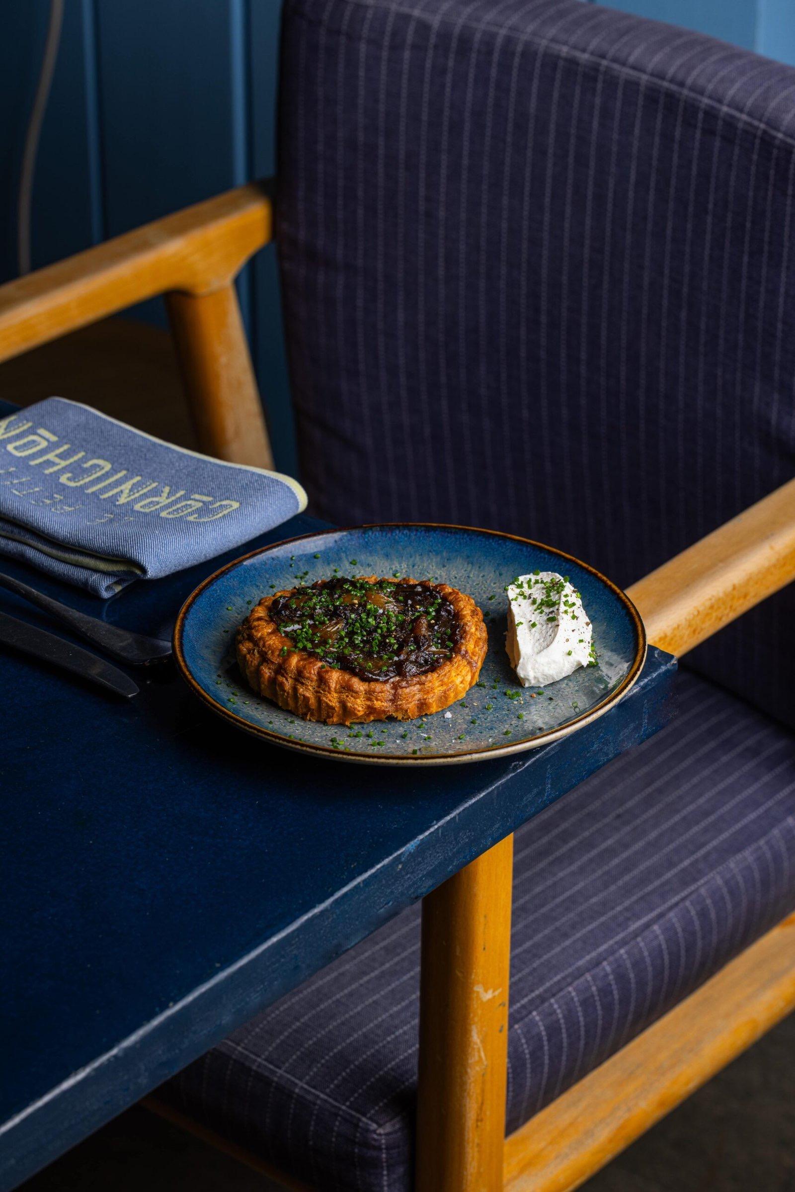 A tart on a blue plate beside a folded napkin on a navy banquette
