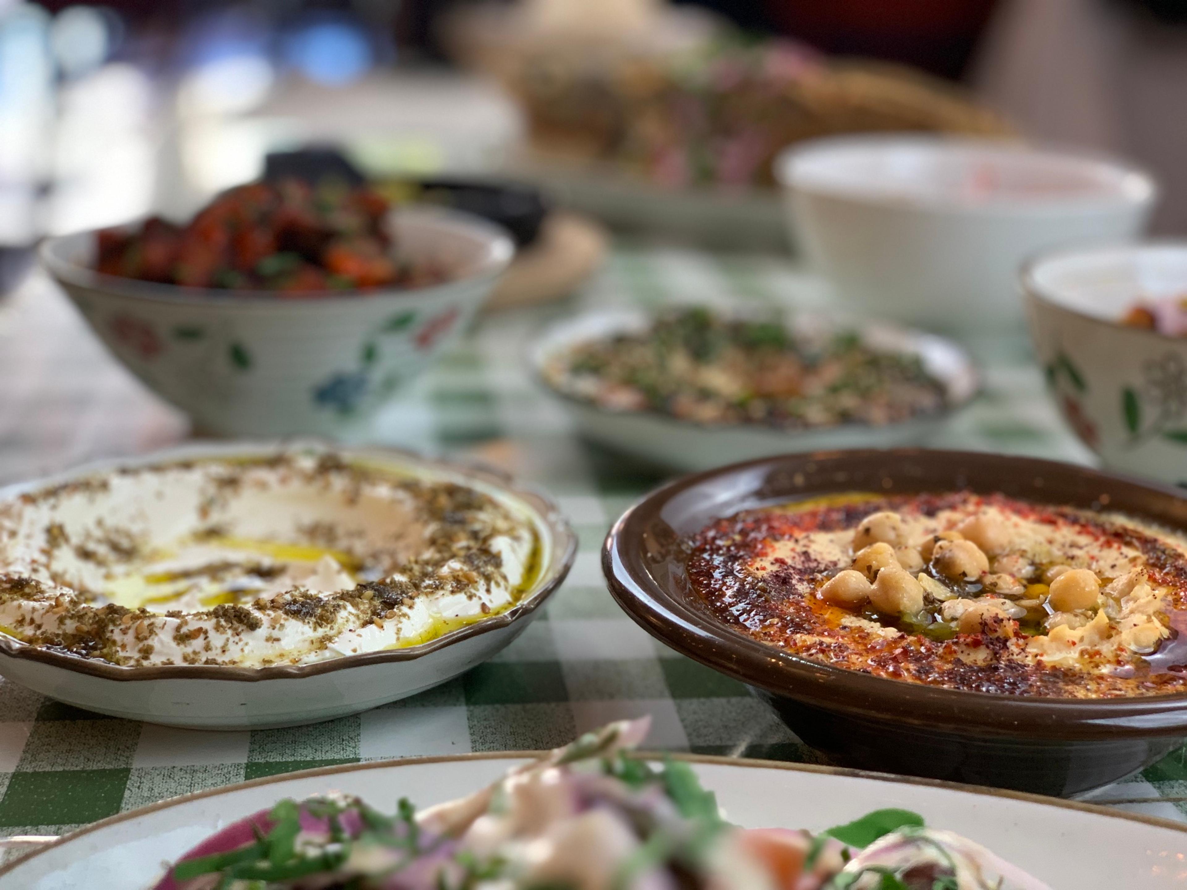 A spread of mezze in patterned bowls on a green gingham tablecloth