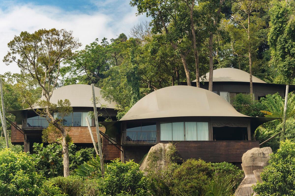 Two dome-roofed villas with glass walls standing among trees.