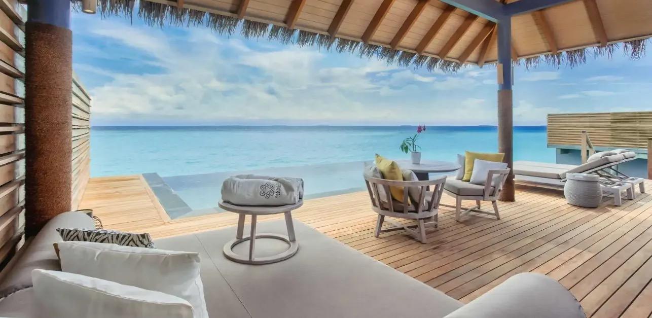 a furnished covered deck with sofas and a dining table looking straight out over open sea to the horizon