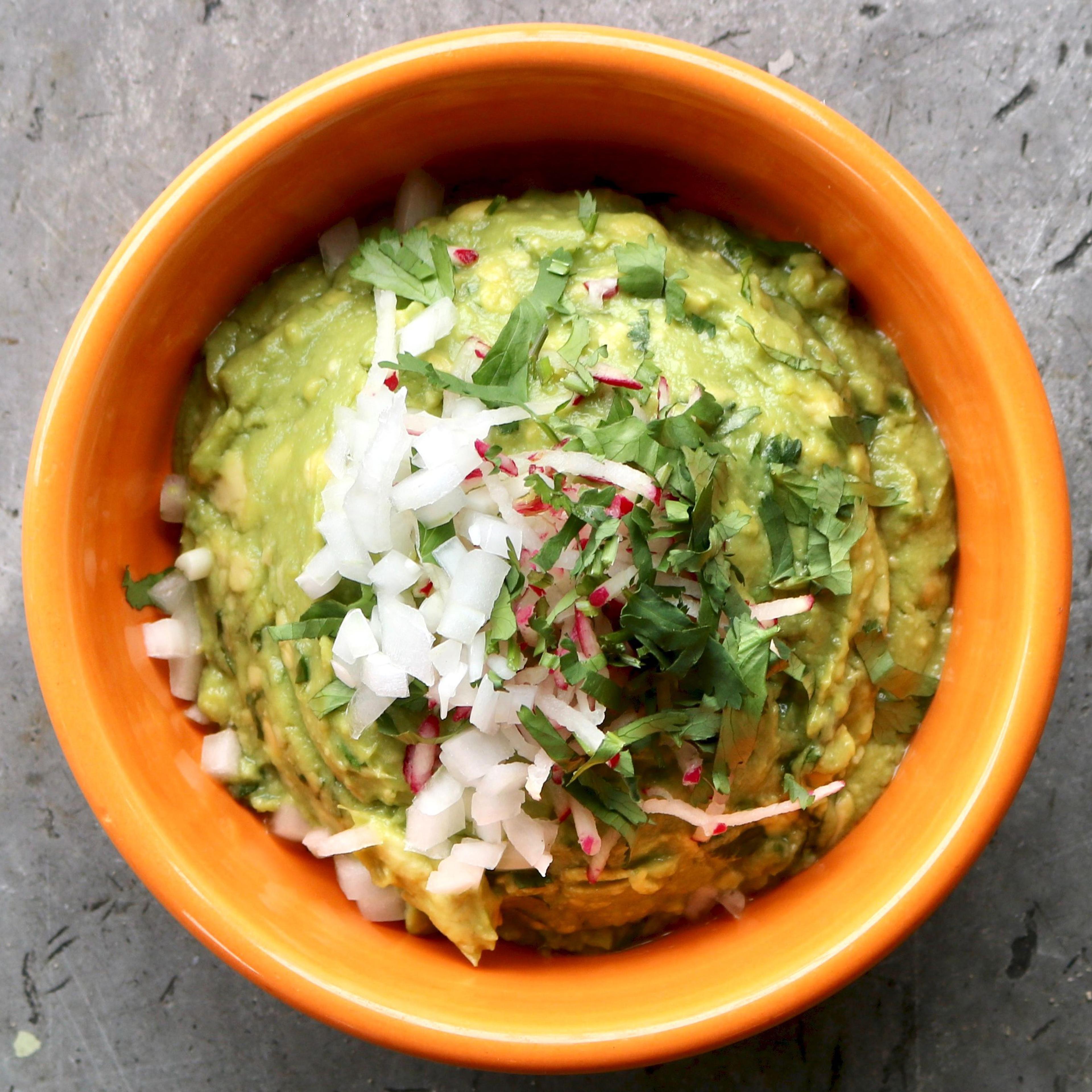 A bowl of guacamole topped with chopped onion and coriander in an orange dish