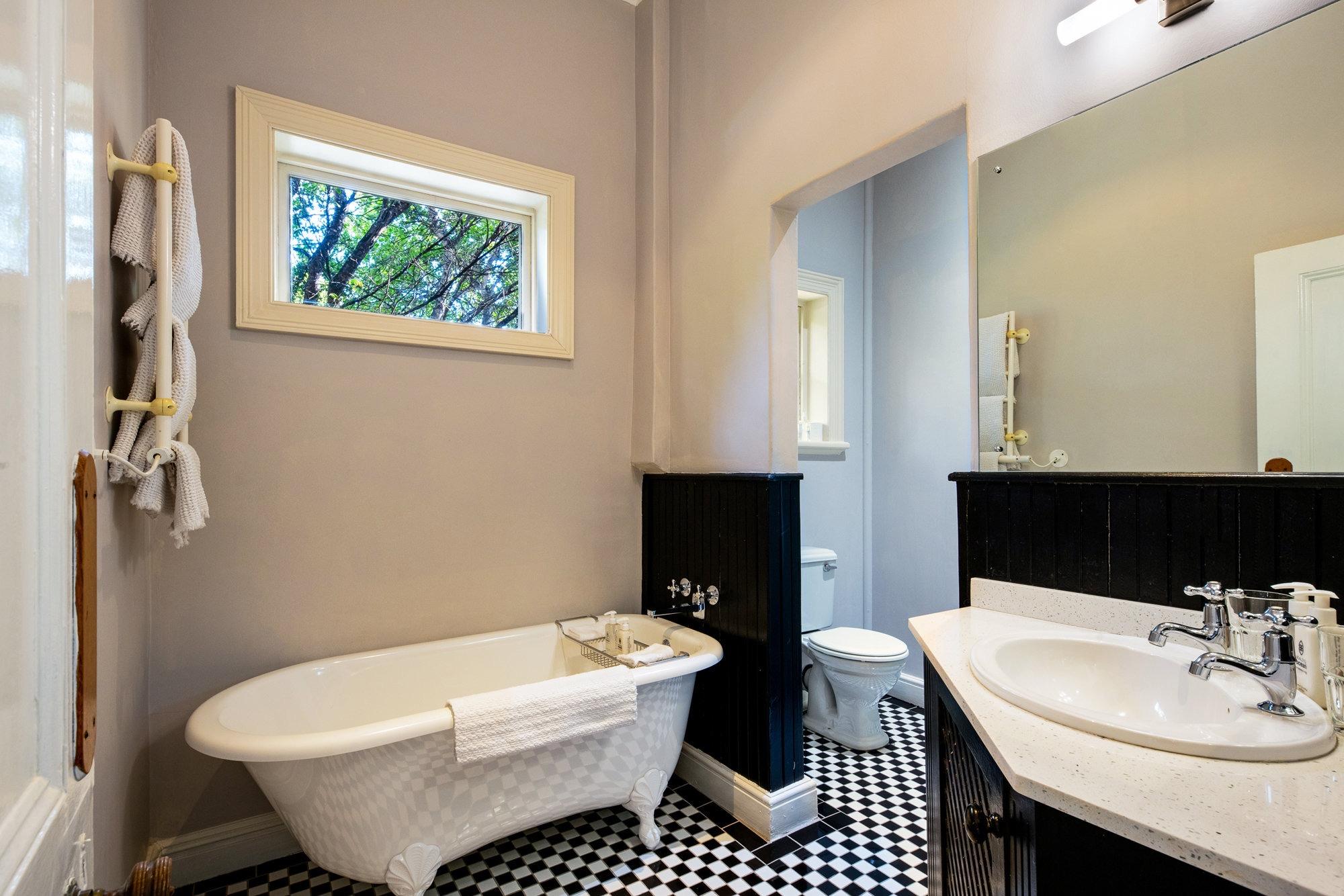 a freestanding white clawfoot bathtub against a black panelled wall, with a black and white checkerboard tiled floor