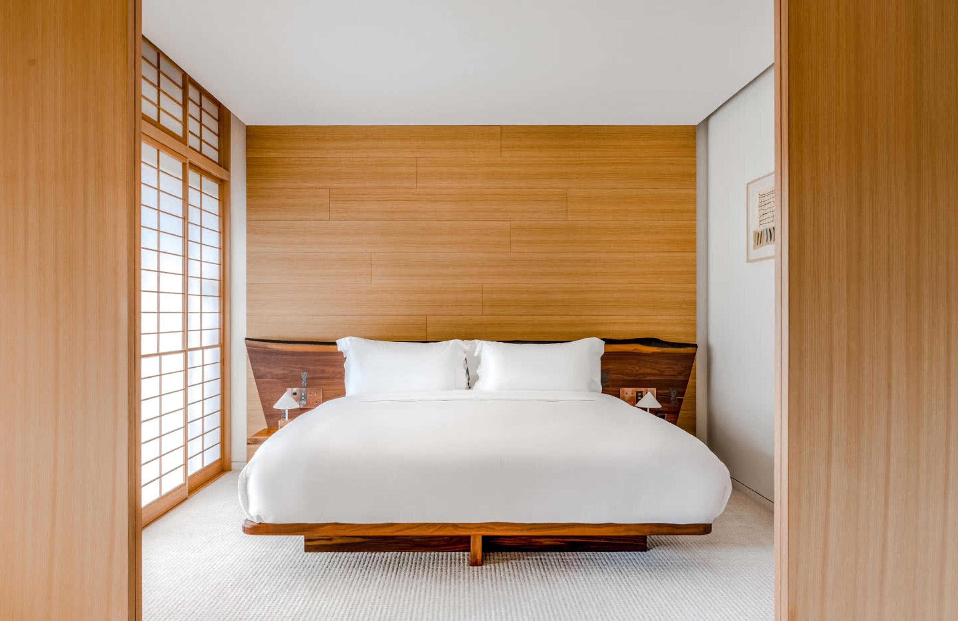 a bedroom with a low wood-framed bed, white linen, and paper sliding doors open toward a wood-panelled wall