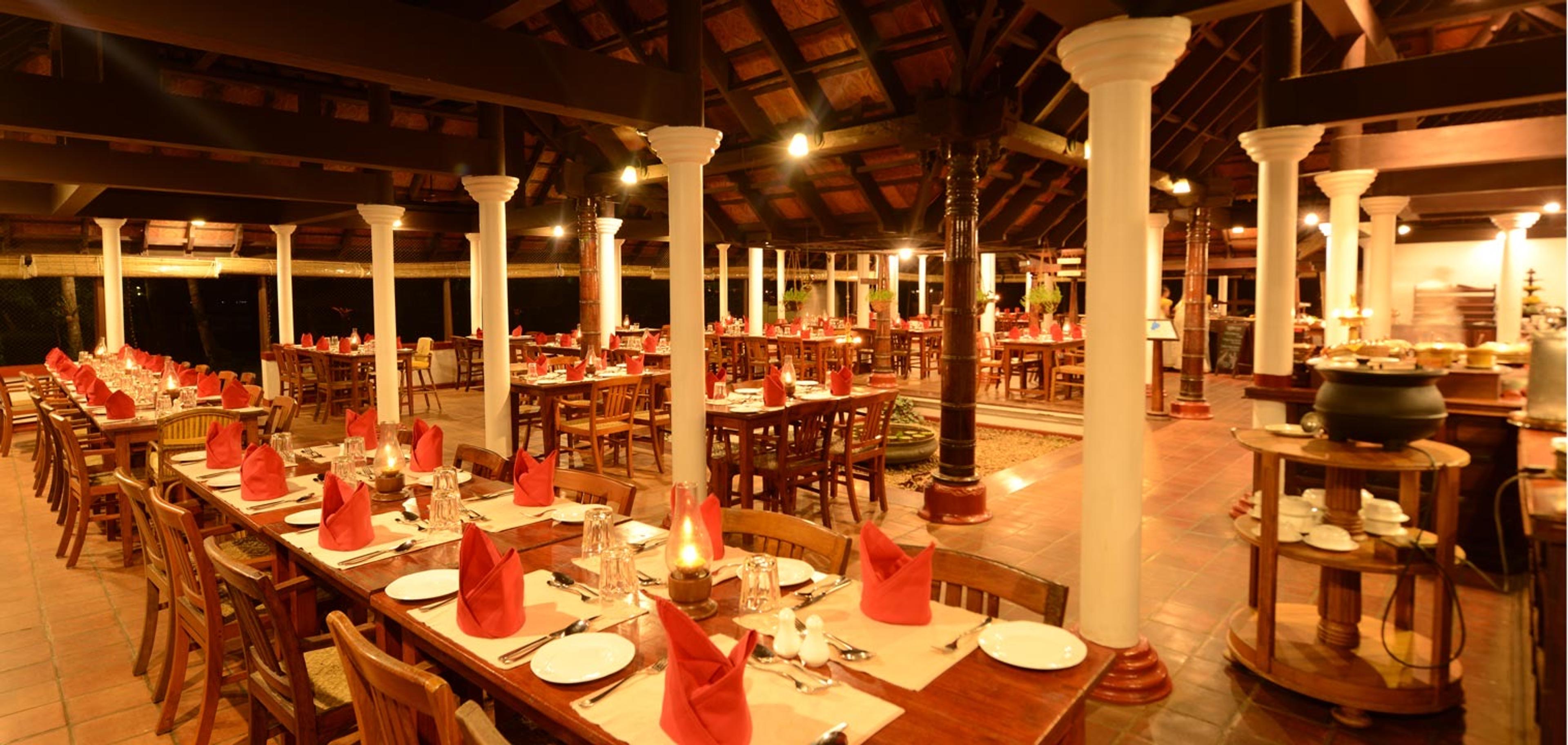 A wide pillared dining hall set with red napkins and glassware, empty before service