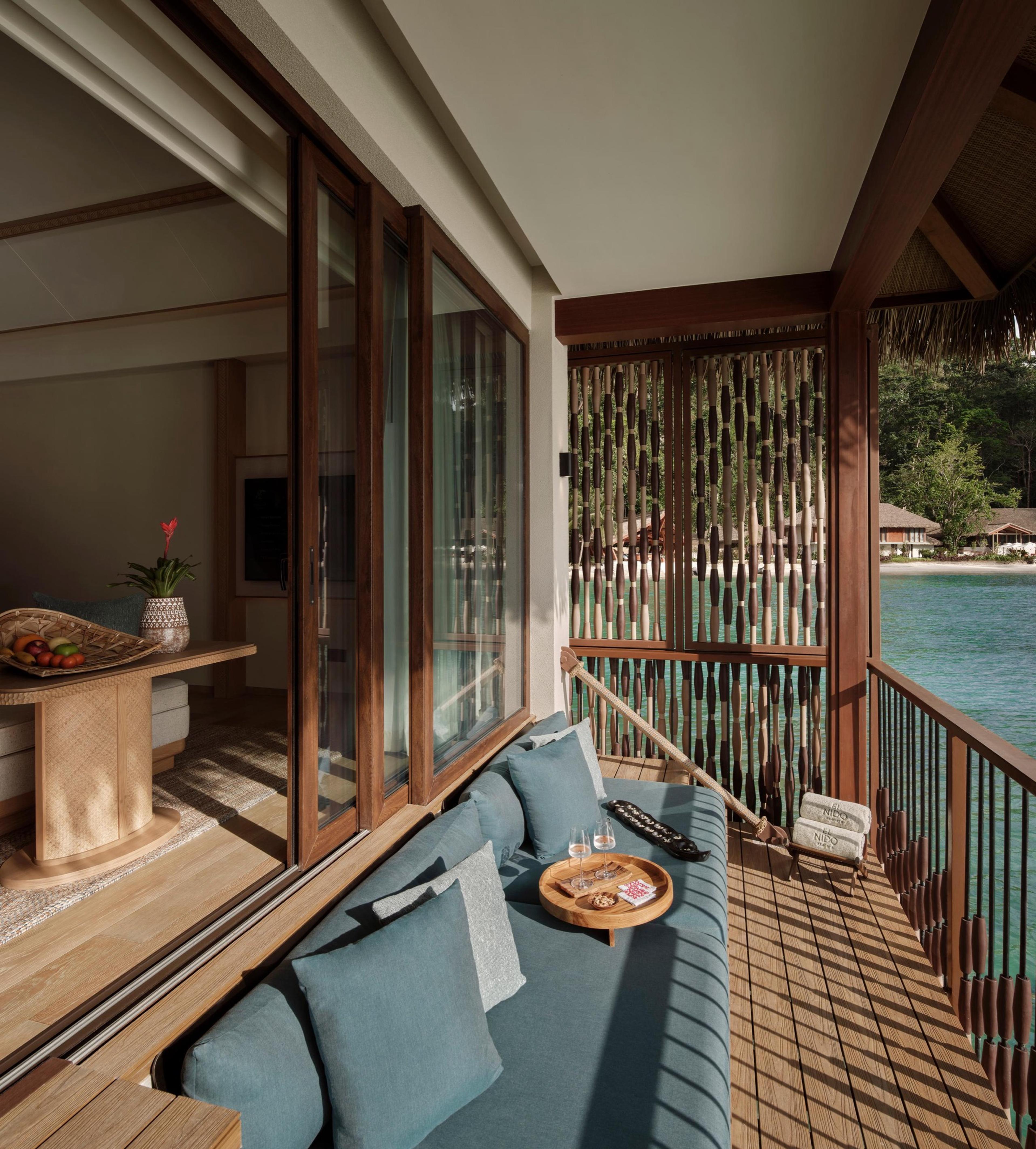 A water villa's sitting area of woven furniture and timber, glass doors open onto a deck over the cove.