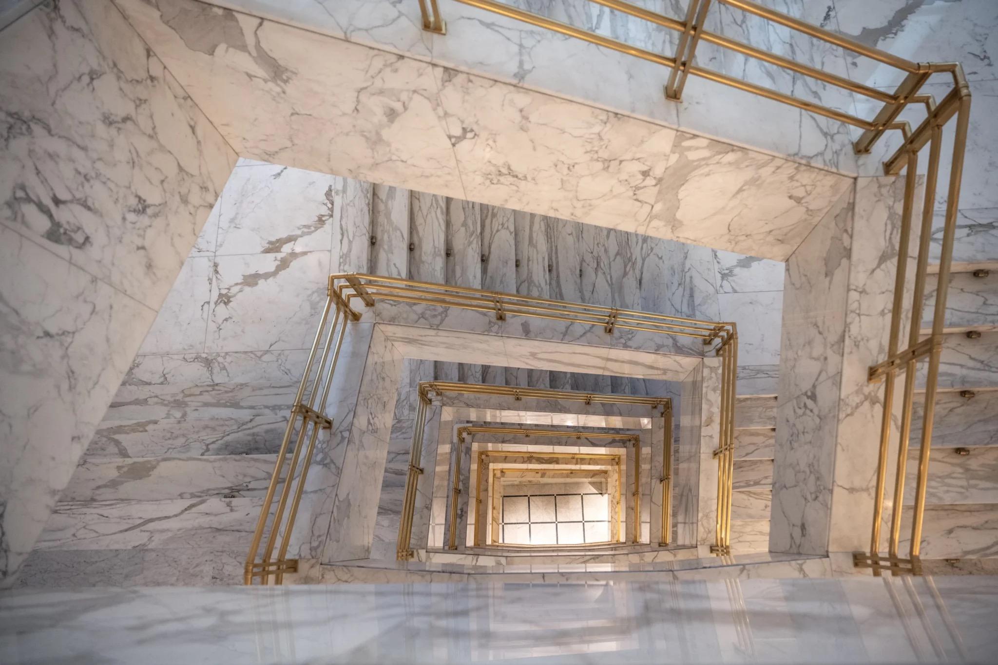 Looking down a marble stairwell with brass handrails that wind round an open well.